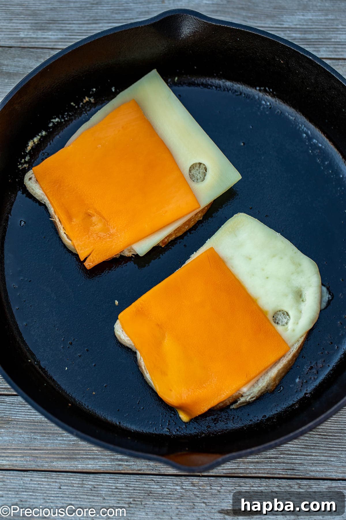 Slices of cheddar and Swiss cheese meticulously arranged on sourdough bread in a skillet, ready for grilling.