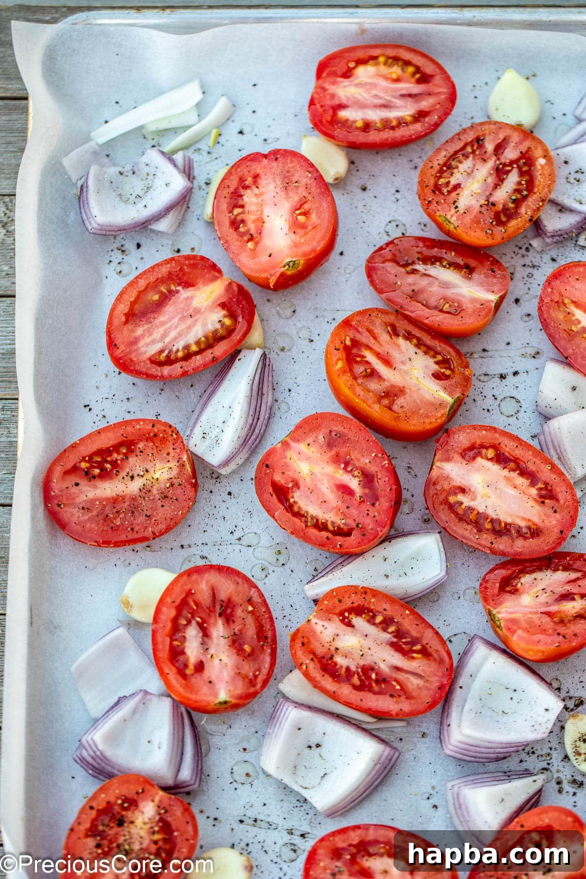 Halved Roma tomatoes, onions, and garlic spread on a sheet pan, ready for roasting.