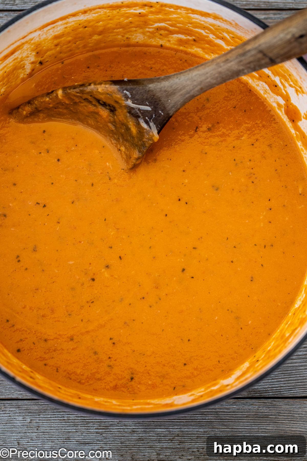 Smooth and creamy tomato soup simmering in a pot with a wooden spoon.