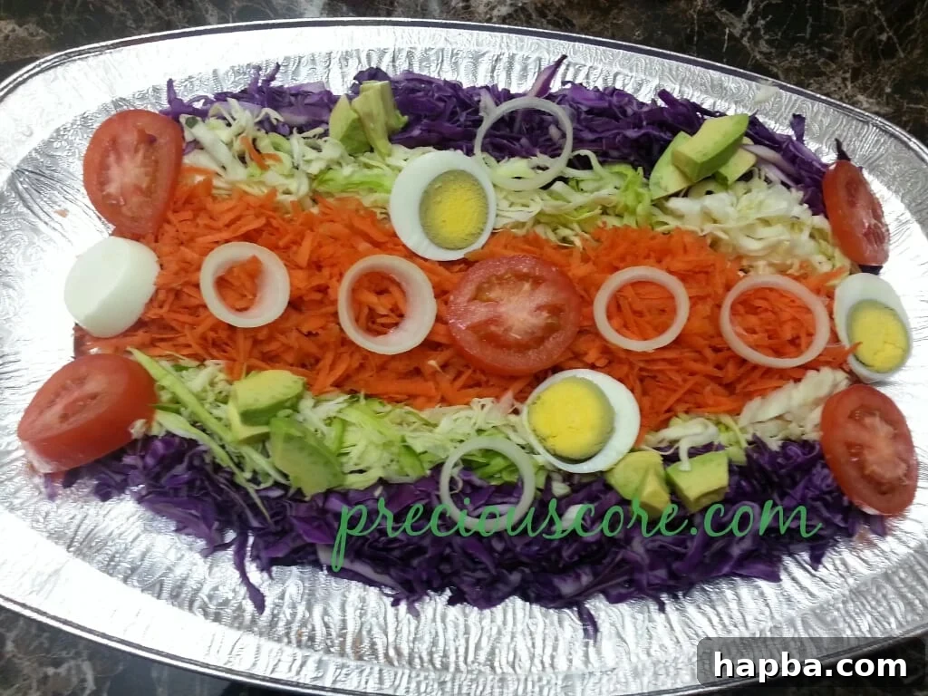 Close-up of a beautifully arranged Cameroon cabbage salad featuring shredded red and white cabbage, carrots, tomatoes, onions, avocado, and hard-boiled egg, ready to be dressed.