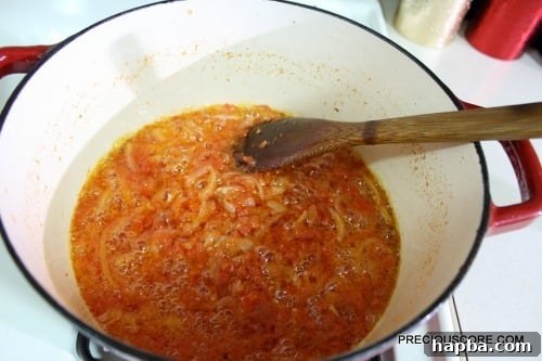 Wooden spoon stirring a pan with tomatoes.