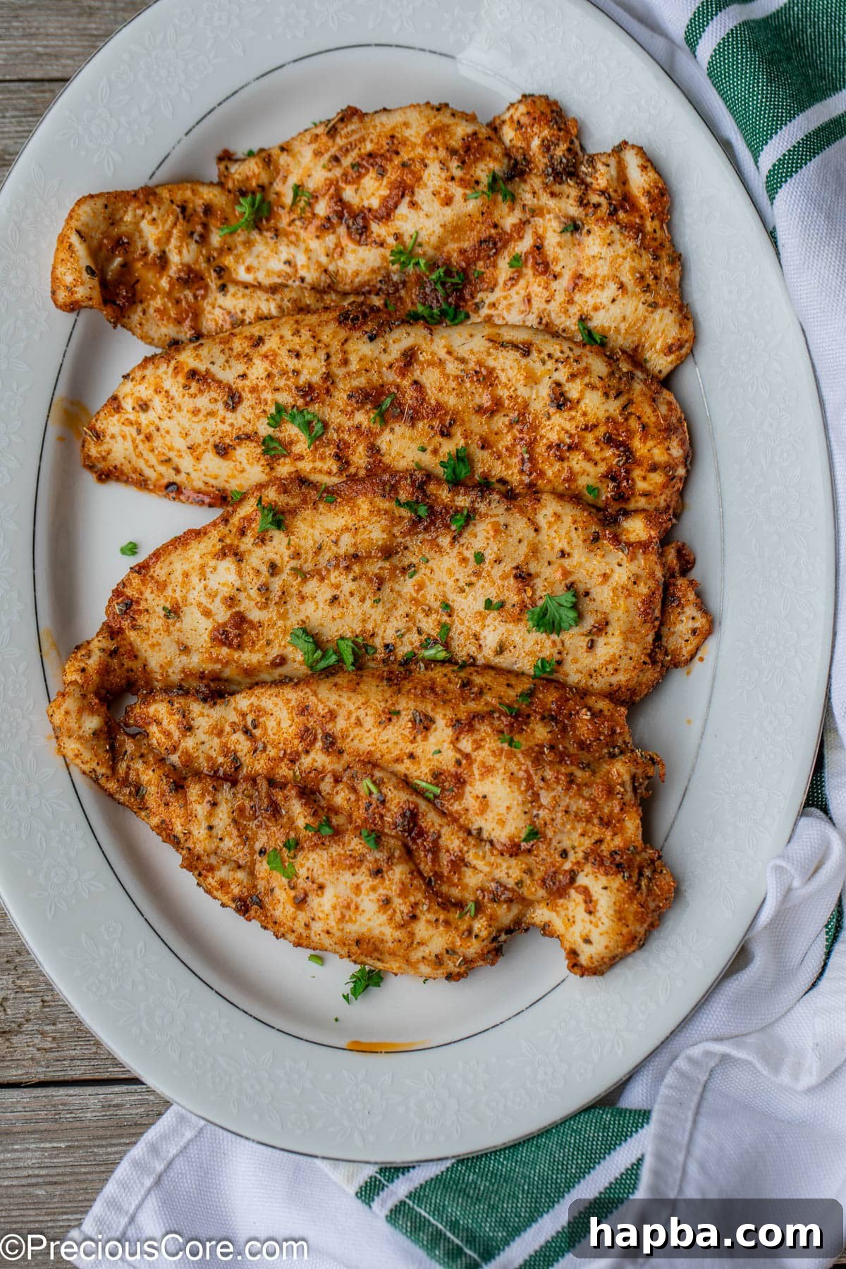 Tender Baked Chicken Cutlets 3 Cooked, golden-brown chicken breasts resting on a white serving plate, garnished lightly with fresh parsley.