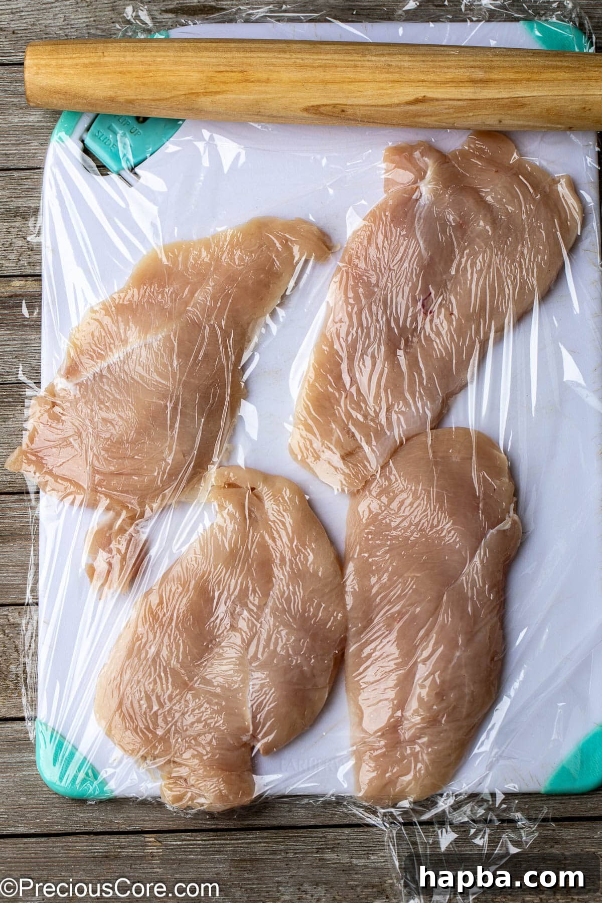 Tender Baked Chicken Cutlets 6 Chicken breasts being flattened with a rolling pin on a chopping board, demonstrating how to create homemade thinly sliced cutlets for even cooking.