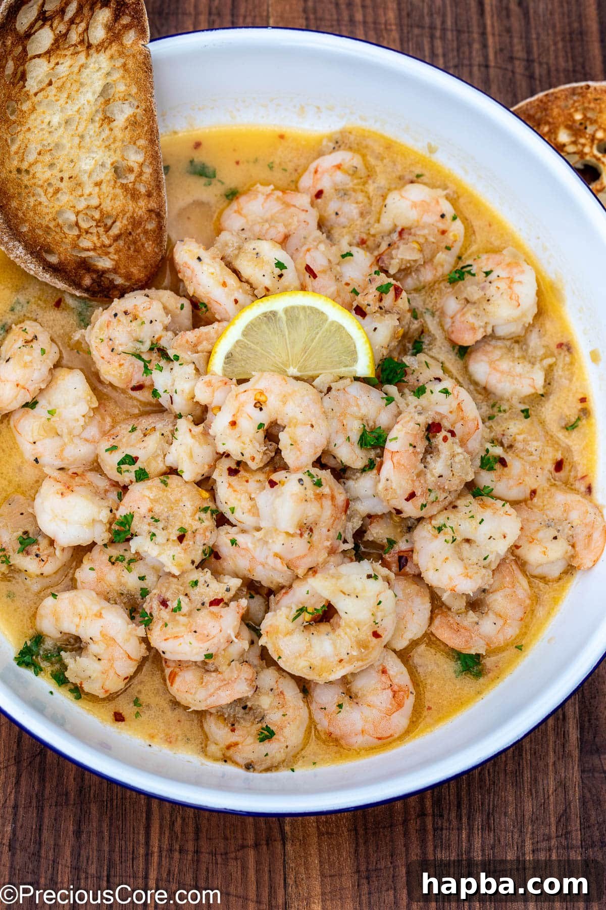 Crusty bread in a bowl of garlicky shrimp in white wine sauce, ready for dipping.