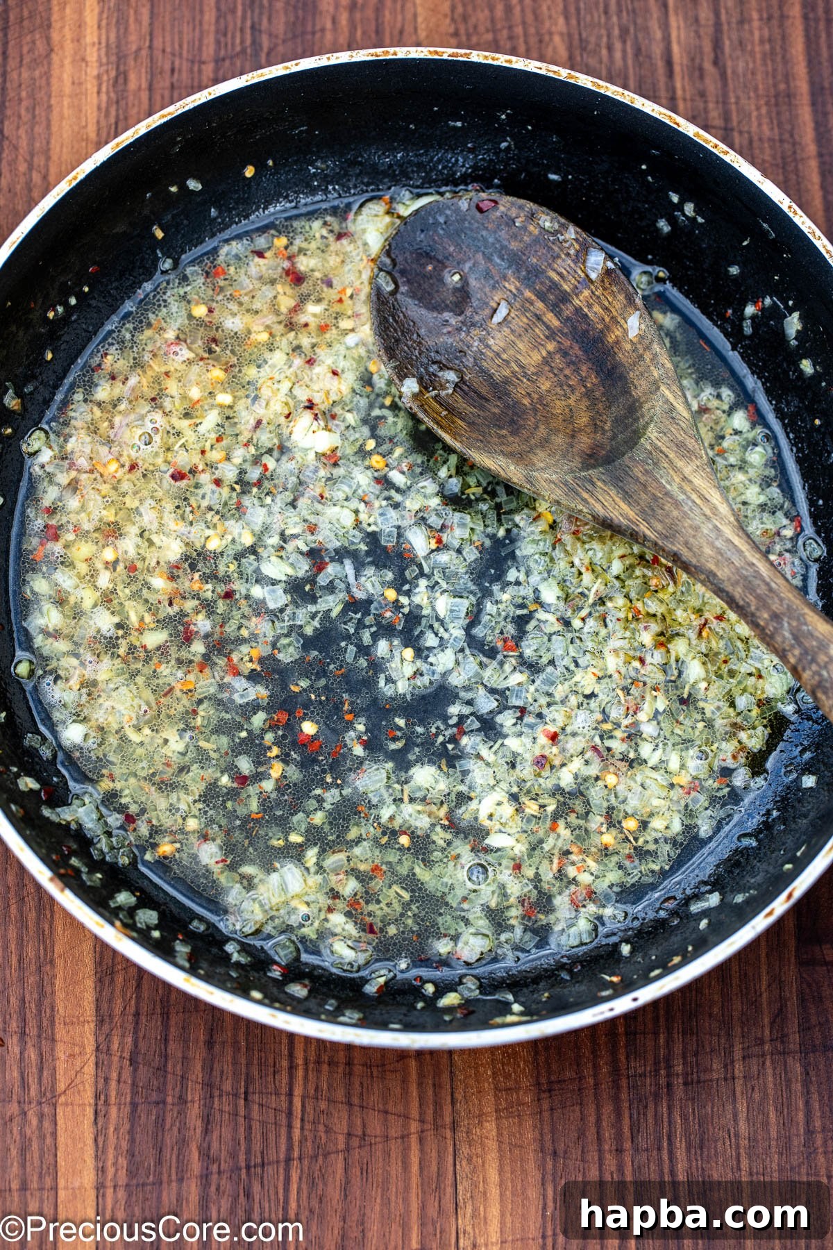 White wine being added to a skillet with sautéed garlic and shallots, creating a fragrant base.