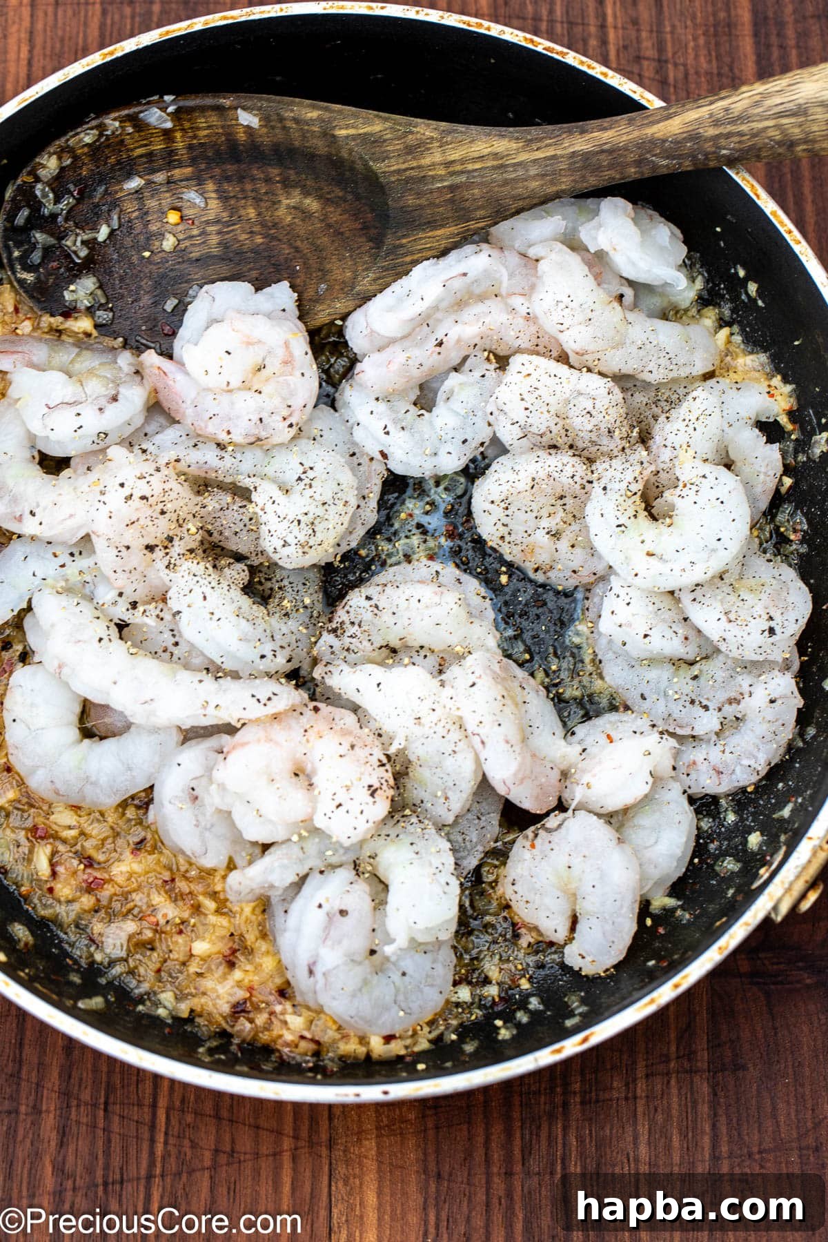Raw shrimp being added to the simmering white wine sauce in a skillet, seasoned with salt and black pepper.