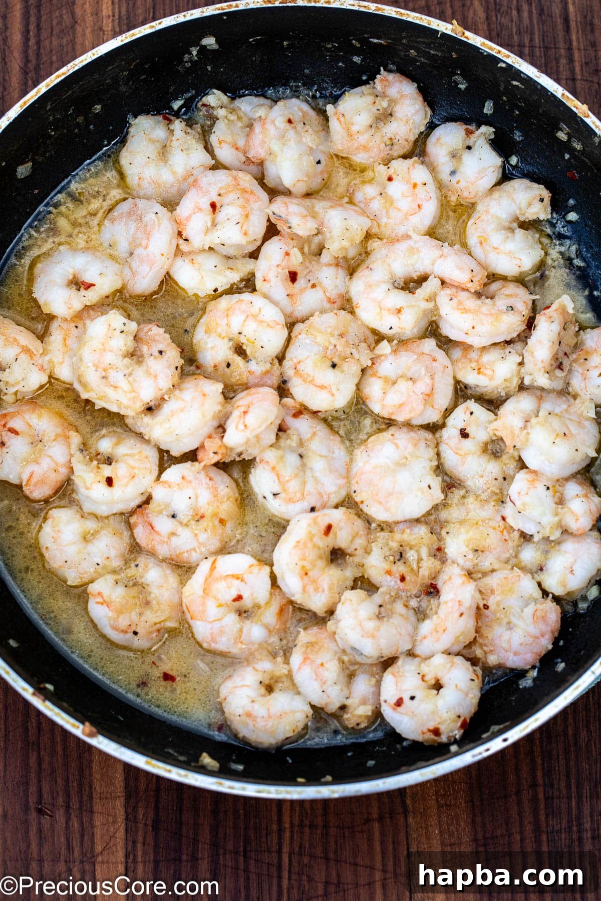Perfectly cooked pink shrimp simmering in a delicious white wine sauce within a skillet.