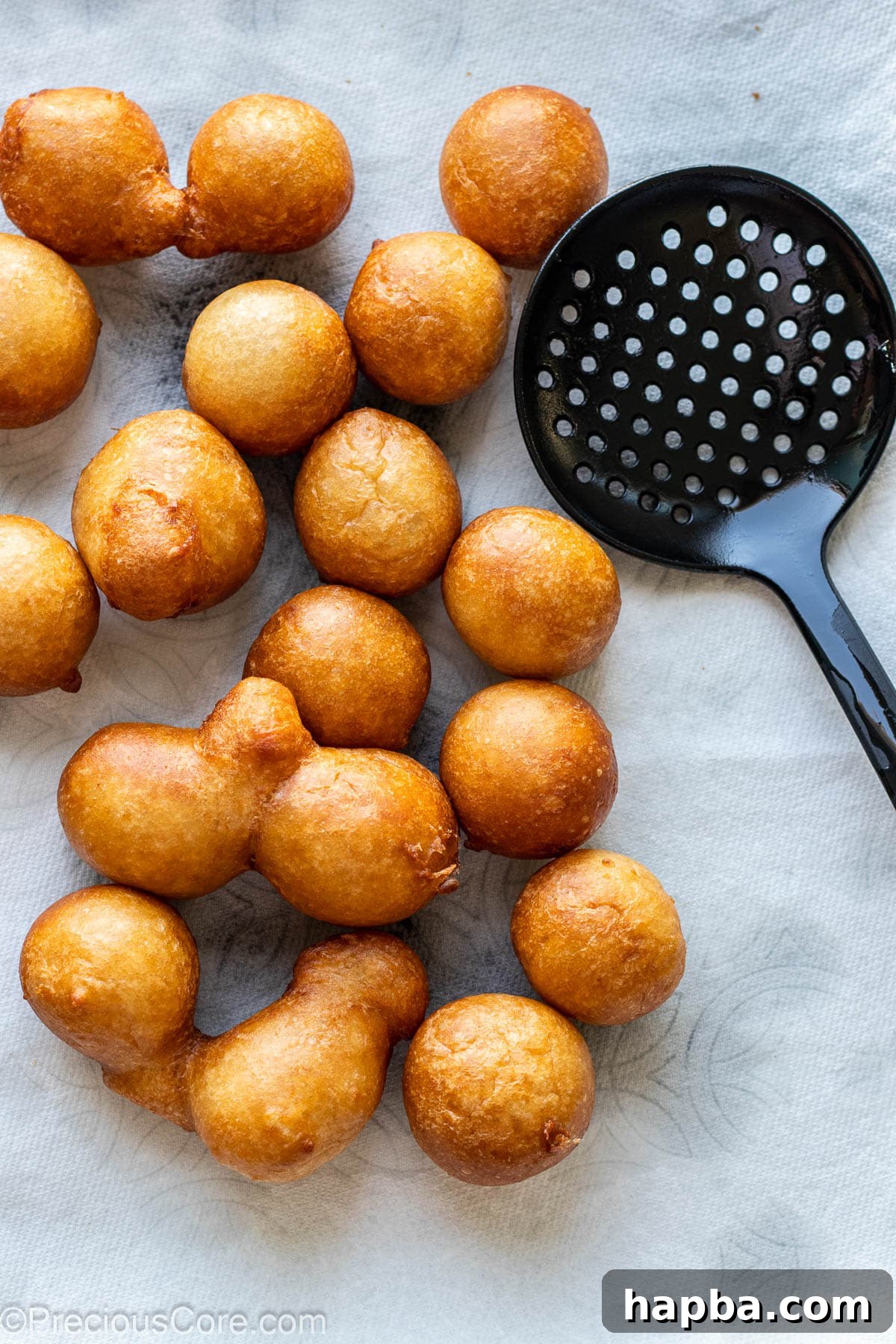 Freshly fried Puff Puff draining on paper towels on a tray, capturing excess oil.