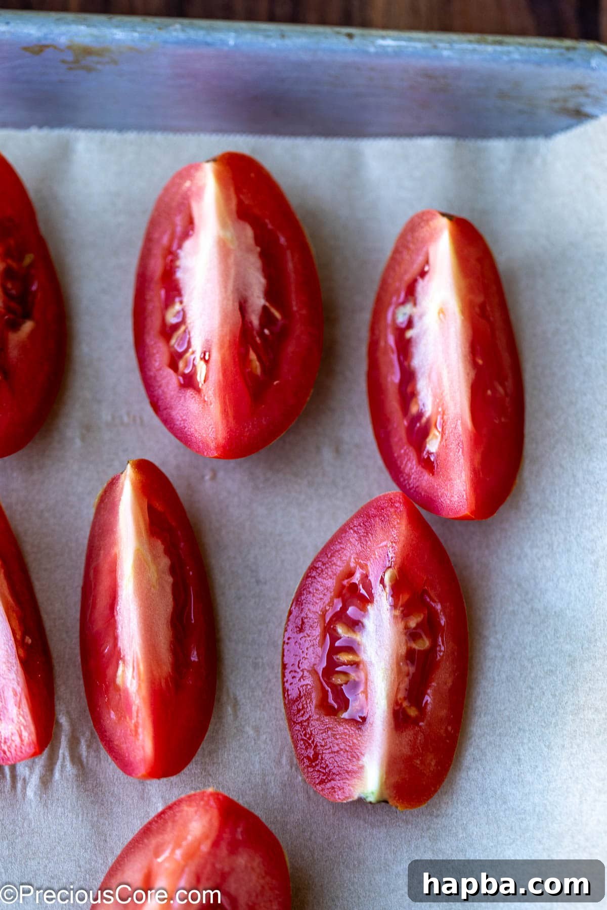 Roma tomatoes cut into quarters on parchment paper.
