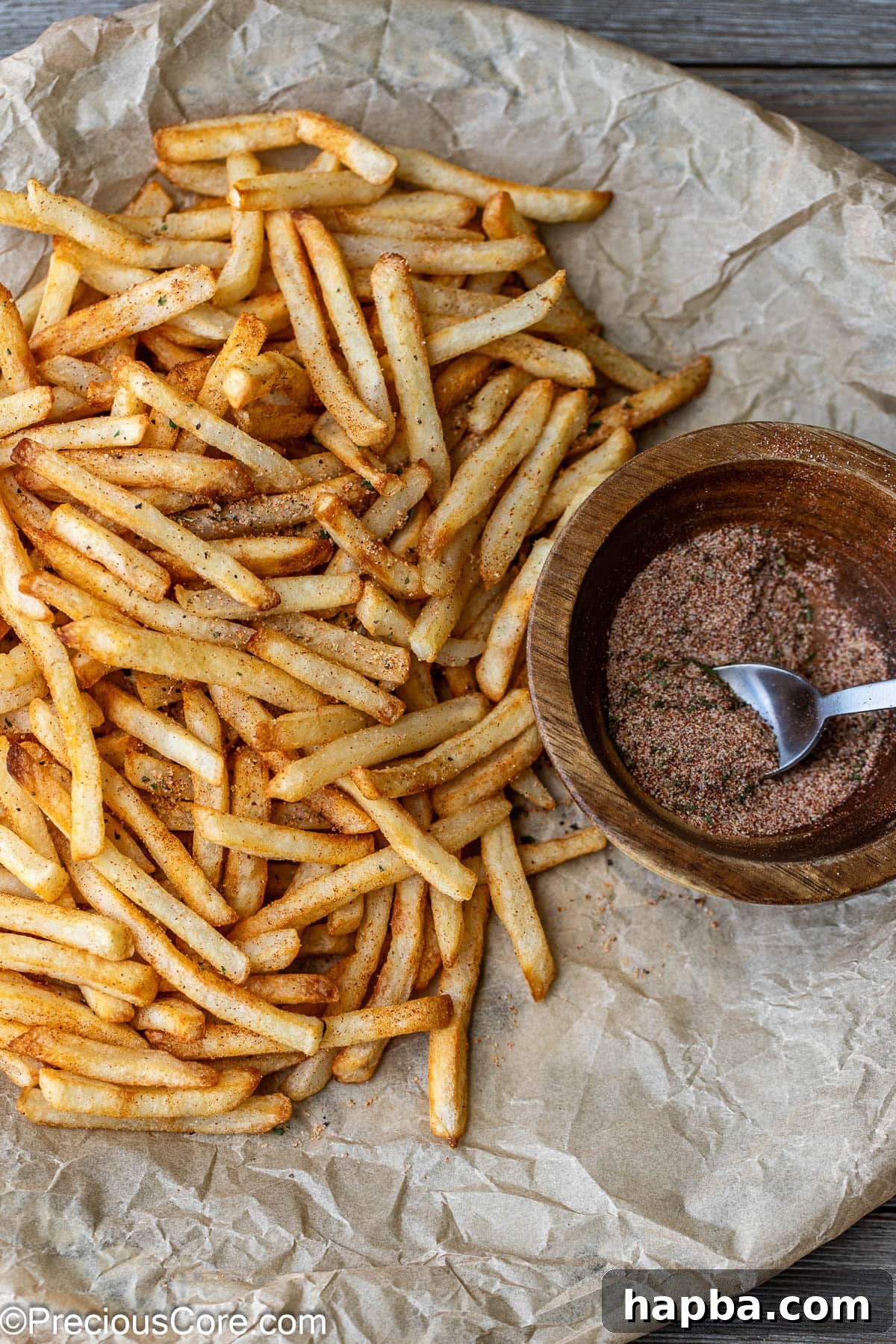 Fries on brown parchment paper with seasoning sprinkled on them.