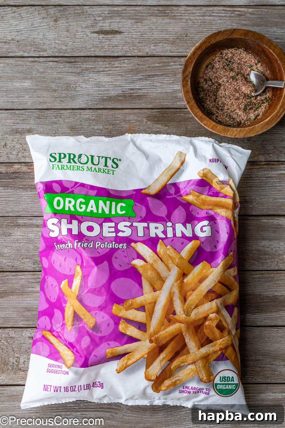 A bag of frozen potato fries next to a small bowl of fry seasoning, ready for cooking.