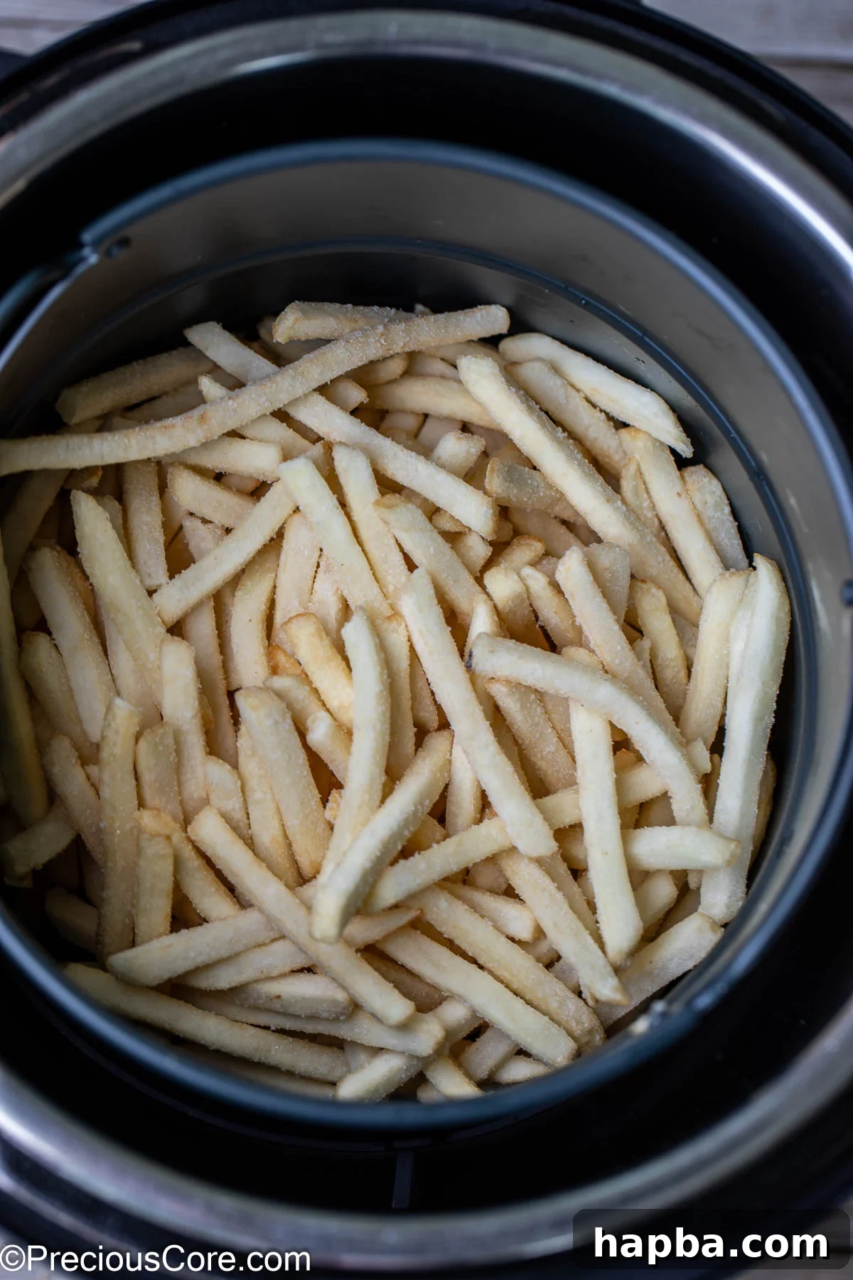 Frozen fries in a round air fryer basket, ready to be cooked to perfection.