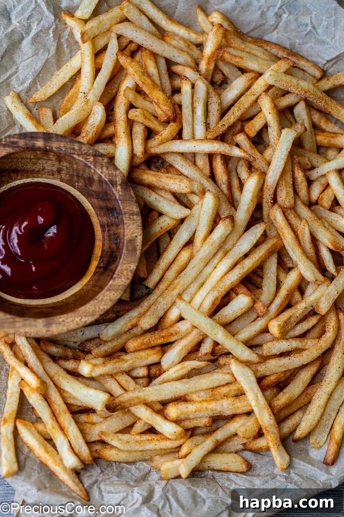 Close-up of golden-brown air-fried fries on a plate, with a small bowl of ketchup for dipping.