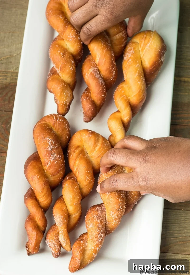 A hand reaching for a golden-brown twisted African doughnut from a generous platter, inviting you to taste these fluffy, sweet pastries.