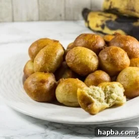 A white plate generously piled with fluffy Plantain Puff Puffs, highlighting their golden hue and appealing texture.