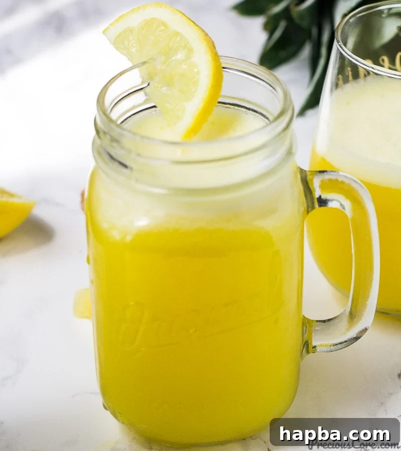 A mason jar filled with bright, golden pineapple ginger juice, elegantly garnished with a half-moon lemon slice on the rim.