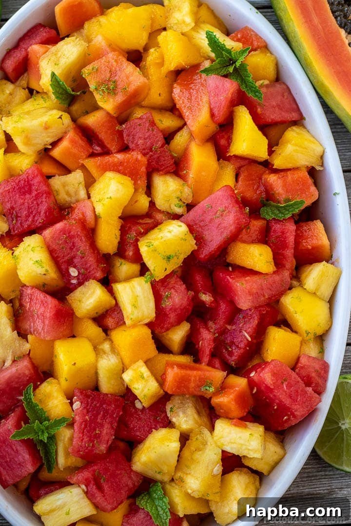 A colorful tropical fruit salad elegantly presented in a white oval serving bowl, brimming with a variety of fresh, diced fruits.