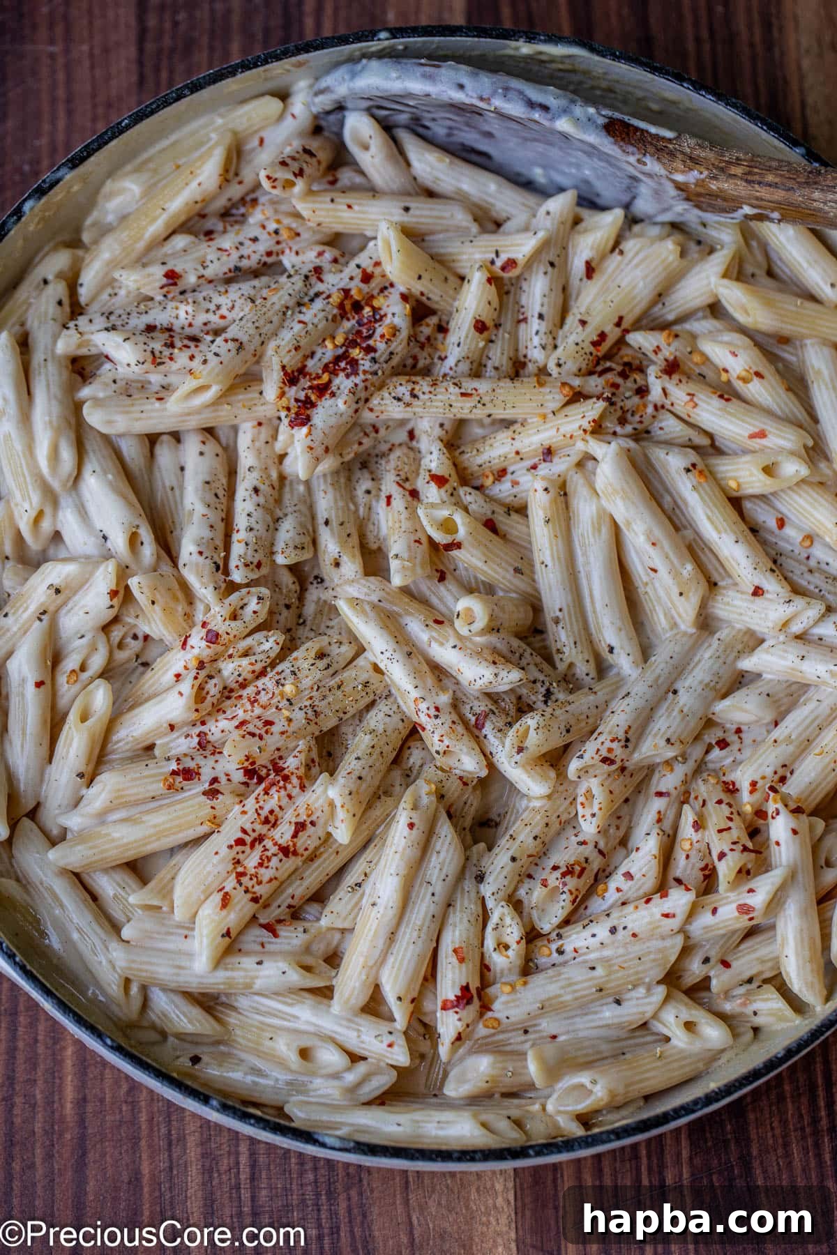 A pot of creamy penne pasta, freshly seasoned with a sprinkle of crushed red pepper flakes and black pepper.