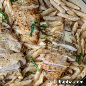 Creamy garlic parmesan pasta topped with tender chicken slices and fresh parsley, presented in a white bowl.