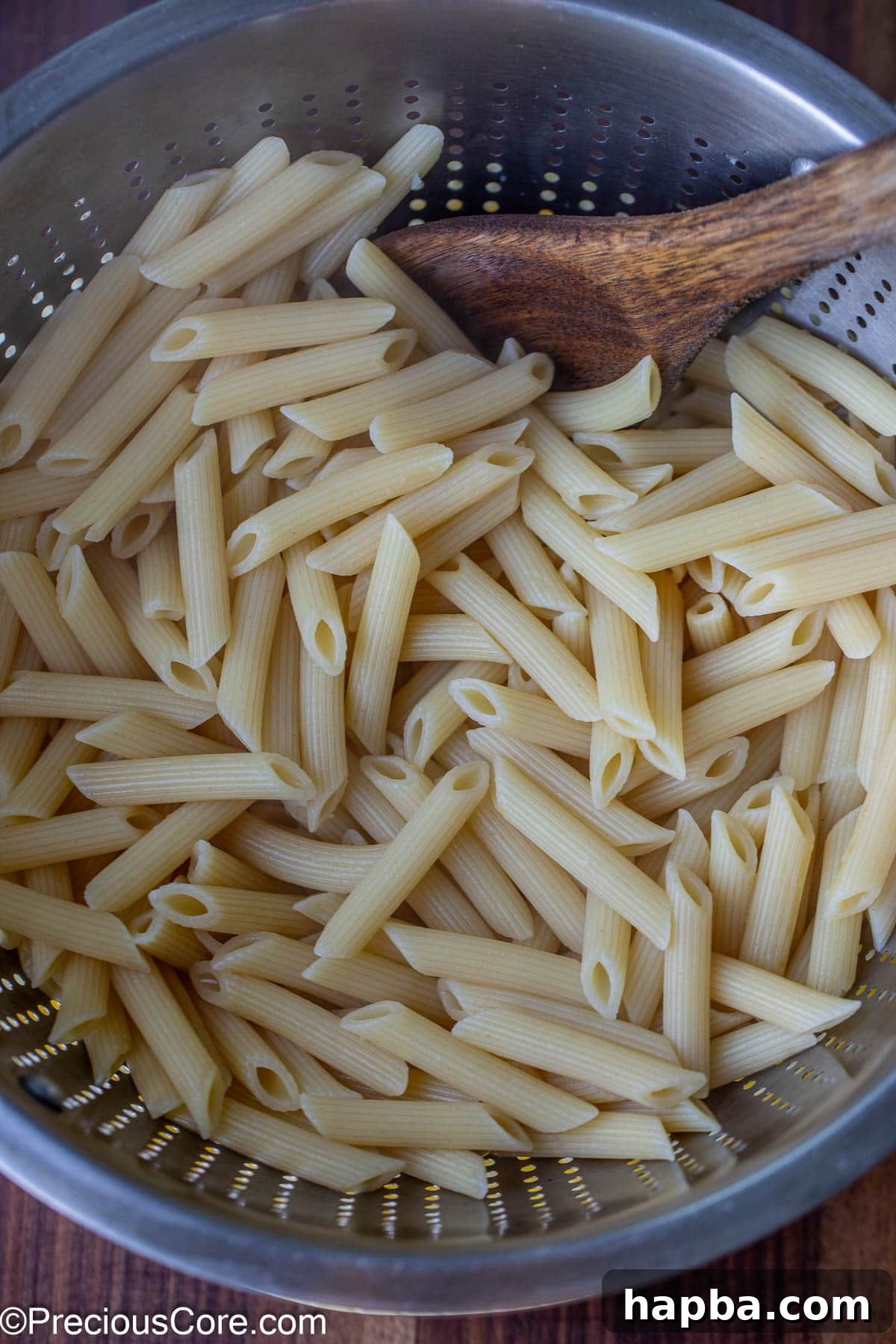 Drained cooked penne pasta resting in a stainless steel colander, glistening and ready to be added to the sauce.