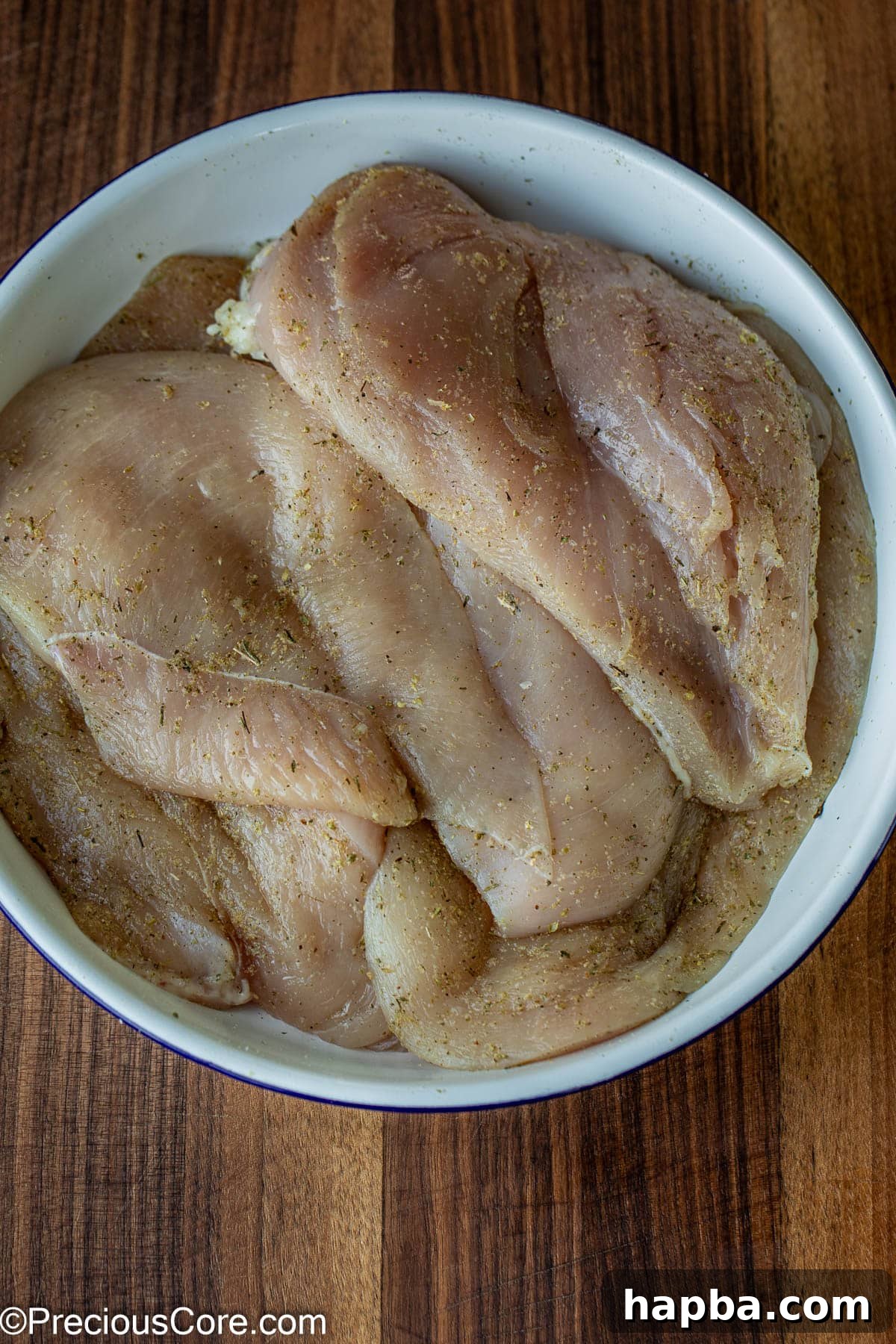 Raw chicken breasts, seasoned liberally with Italian seasoning, garlic powder, and salt, resting in a pristine white bowl.