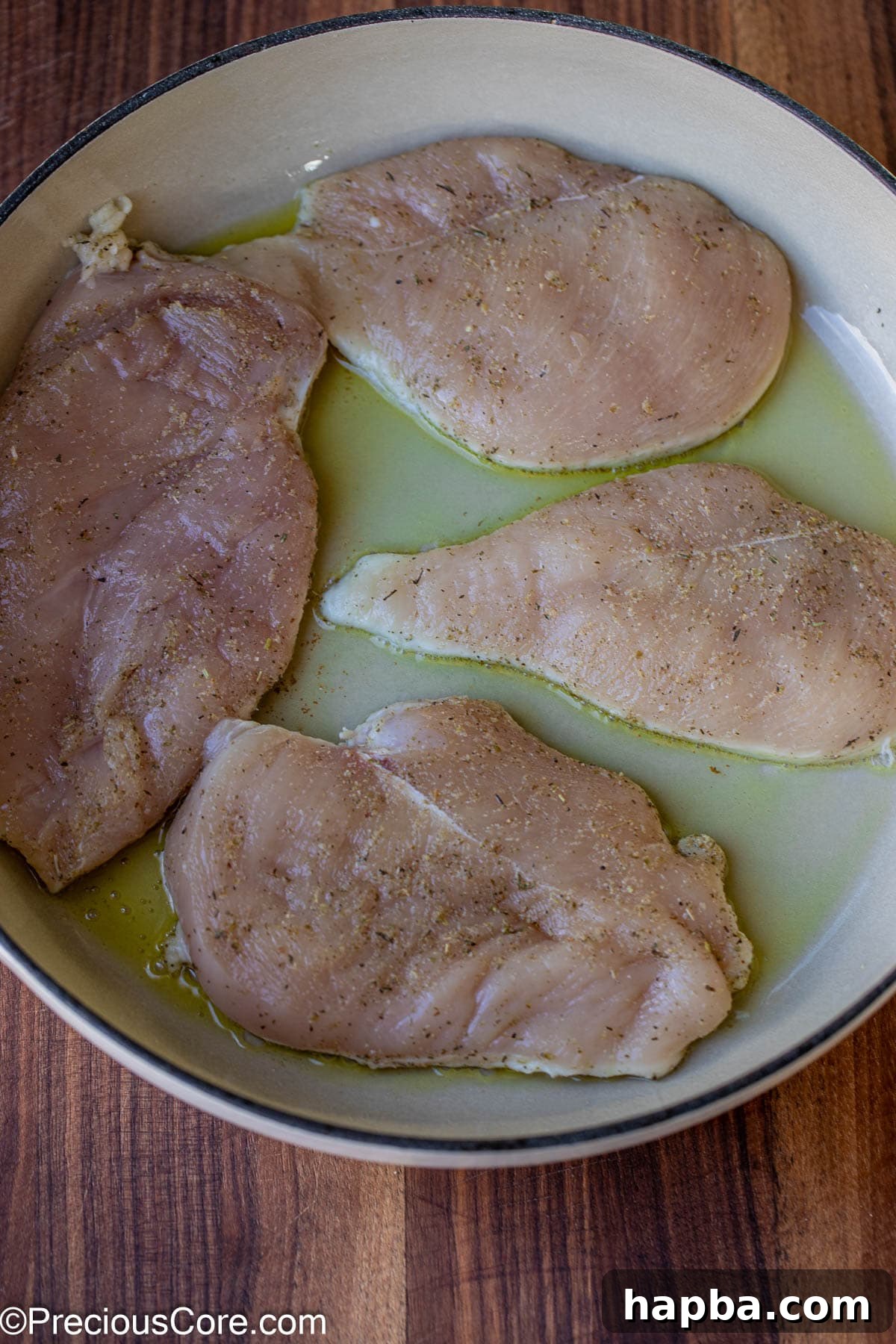 Raw seasoned chicken breasts being carefully placed into a hot skillet with shimmering olive oil.