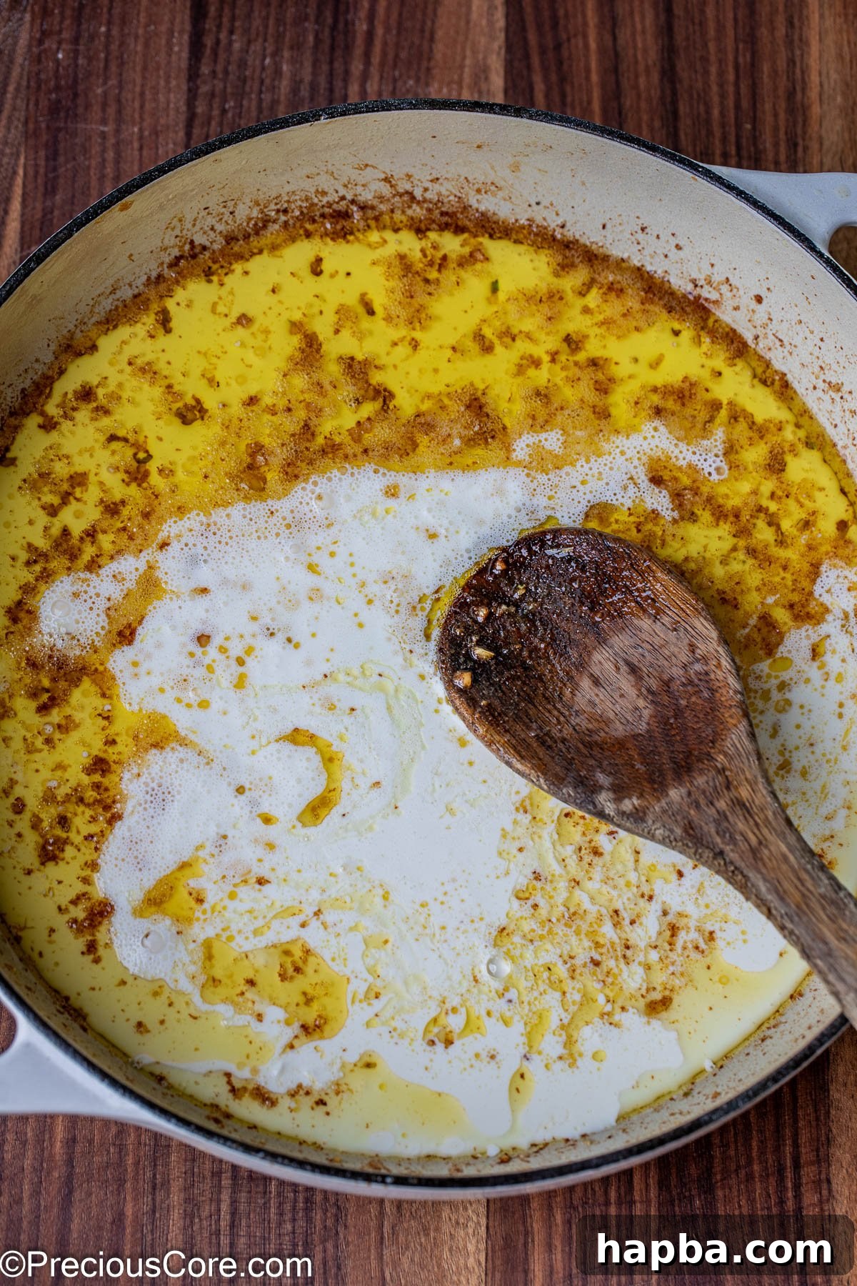Heavy cream being steadily poured into a skillet containing melted butter and sautéed garlic, beginning the sauce creation.