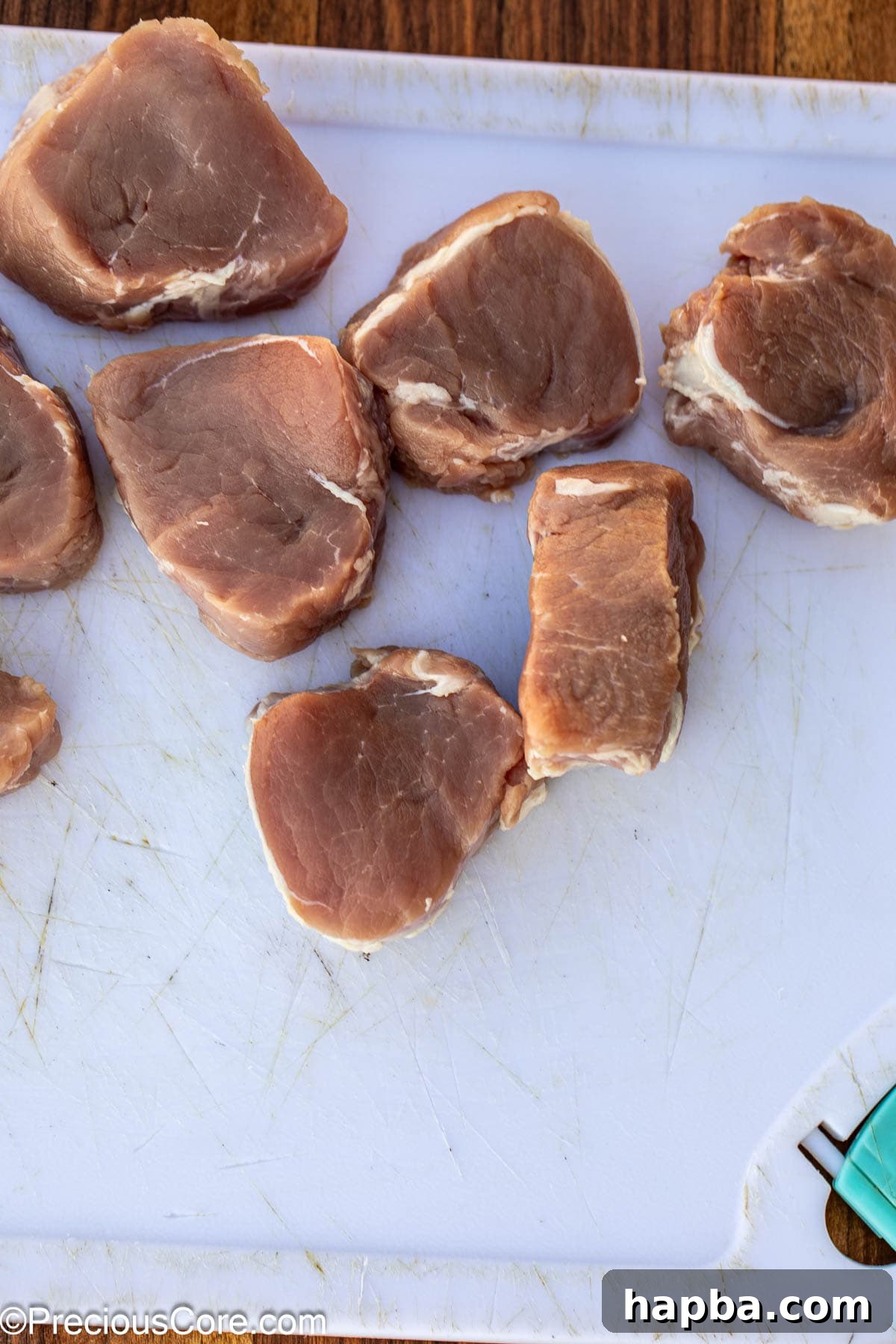 Pork tenderloin being sliced on a chopping board into uniform medallions.