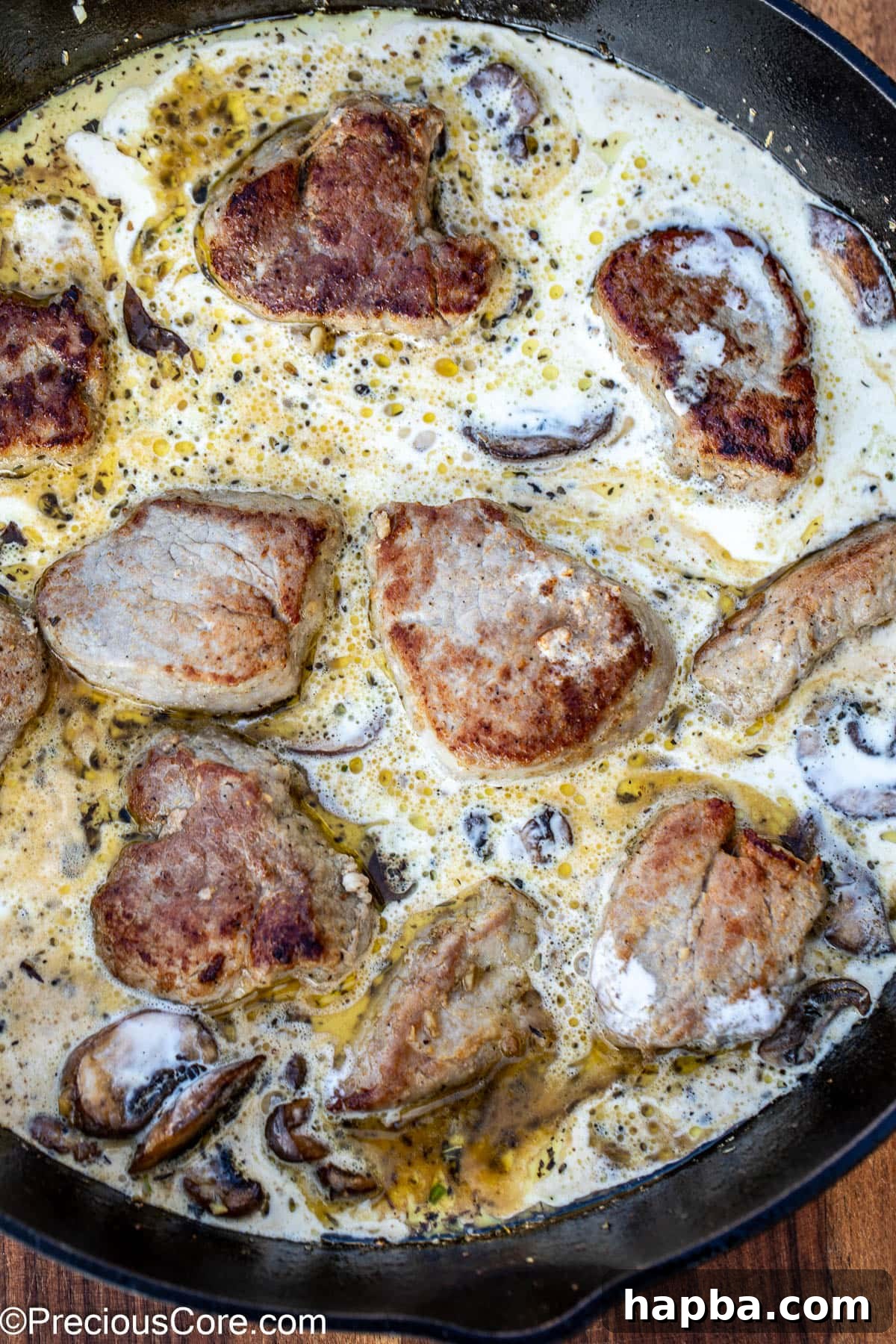 Creamy mushroom sauce with round slices of pork tenderloin simmering in a skillet.