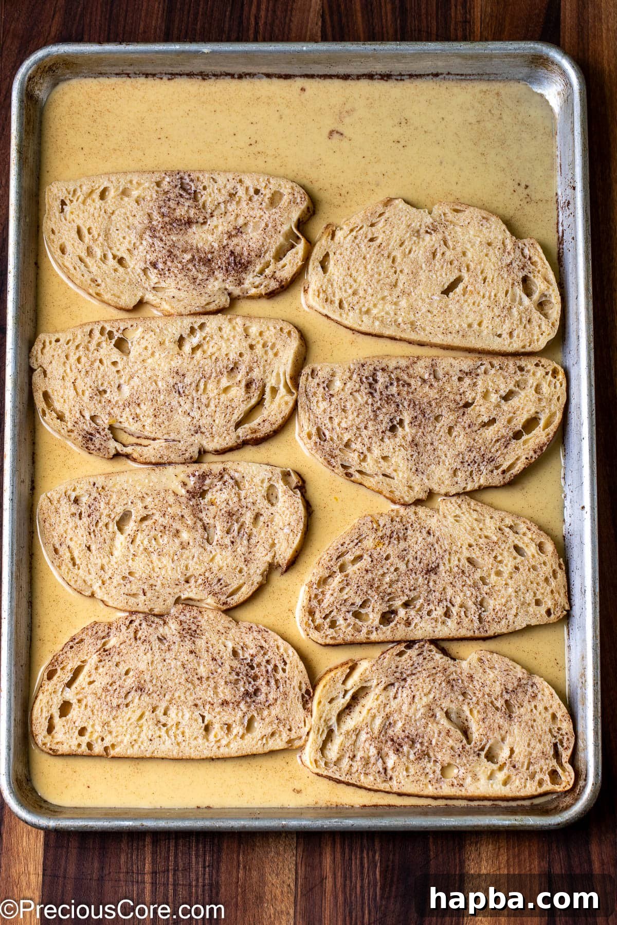 Bread slices soaking in custard on a baking sheet.