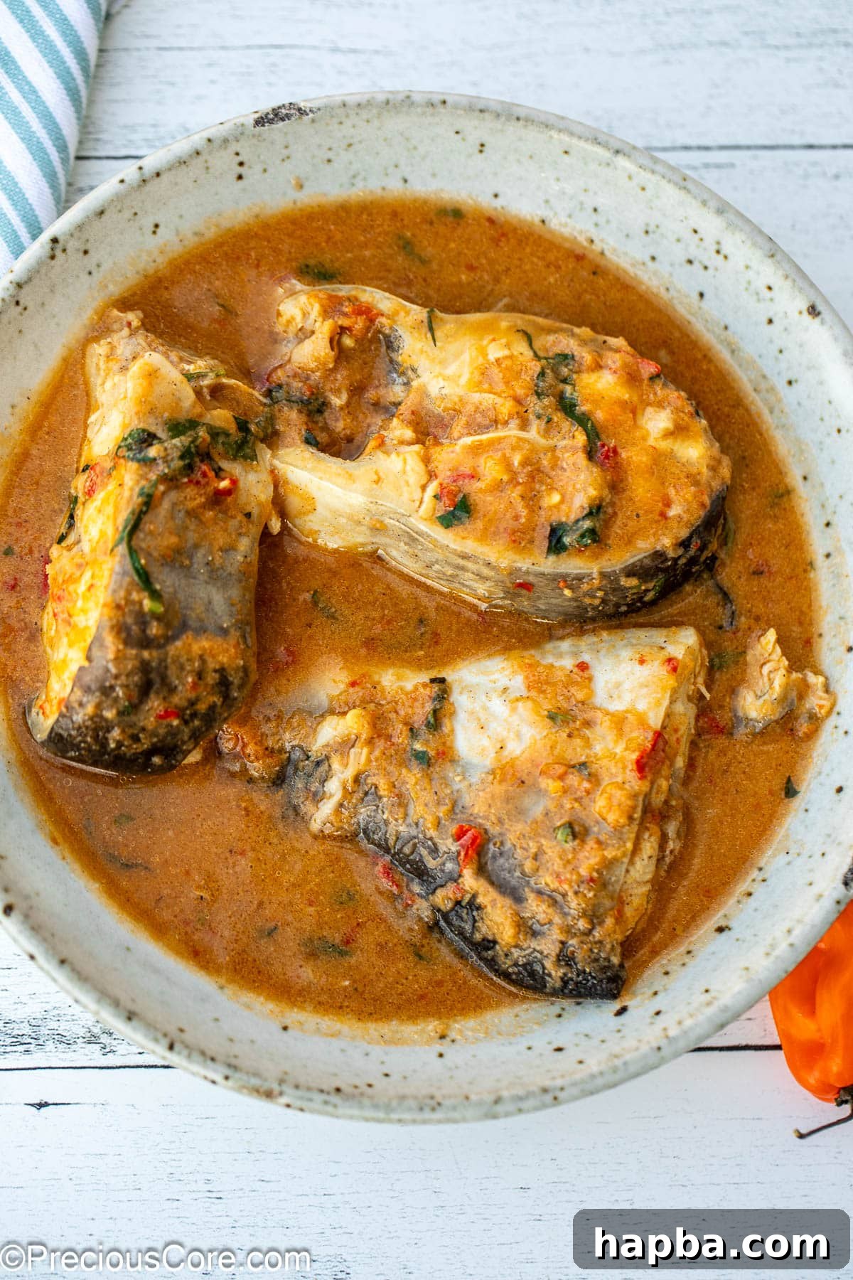 A bowl with three steaks of catfish in pepper soup, showcasing the vibrant broth and tender fish.