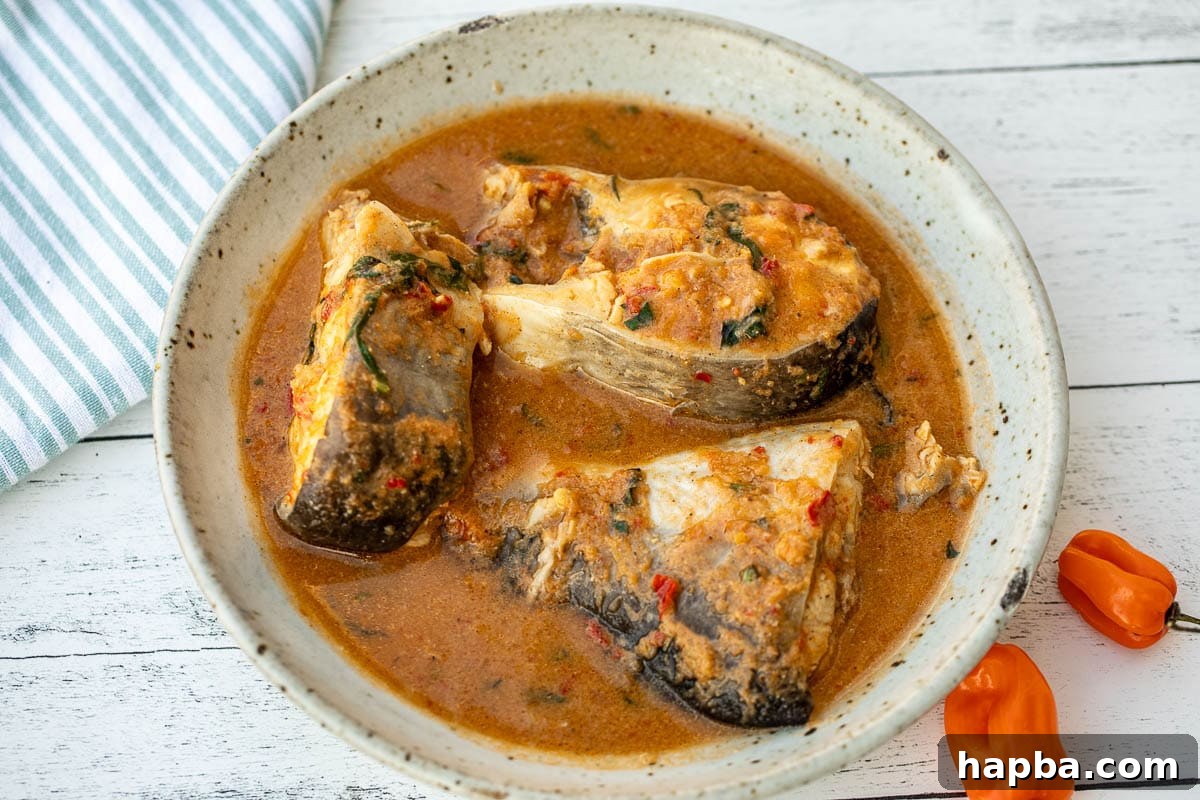 Landscape photo of Nigerian pepper soup simmering gently in a pot, rich with spices and fish.