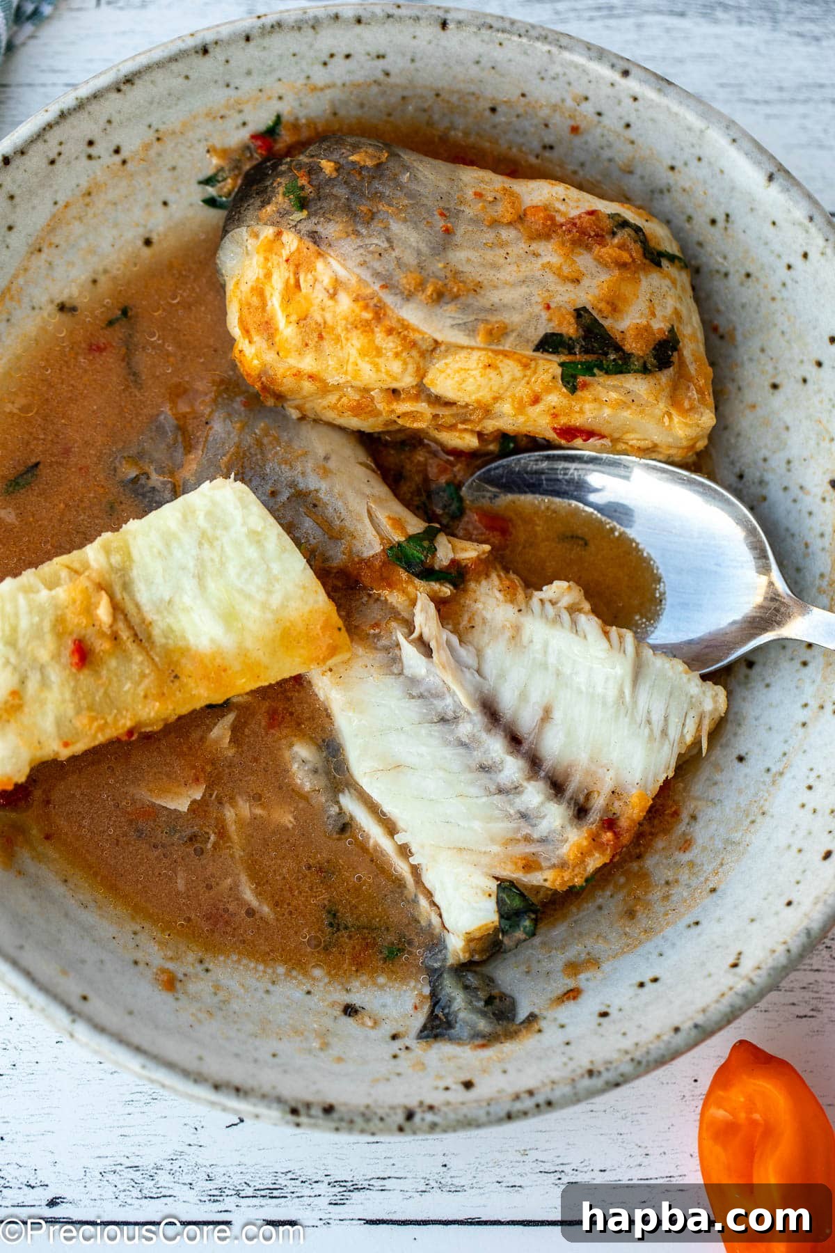 A close-up of a fish tail in a vibrant broth, served alongside chunks of African white yam, ready to be enjoyed.