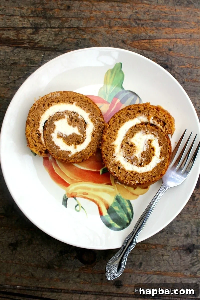 Autumn Spiced Pumpkin Roll 2 Two slices of pumpkin roll cake on a plate with a fork, elegantly presented.