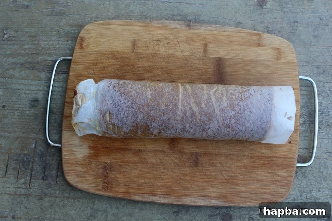 Autumn Spiced Pumpkin Roll 13 Warm pumpkin cake rolled with parchment paper on a cutting board, cooling.