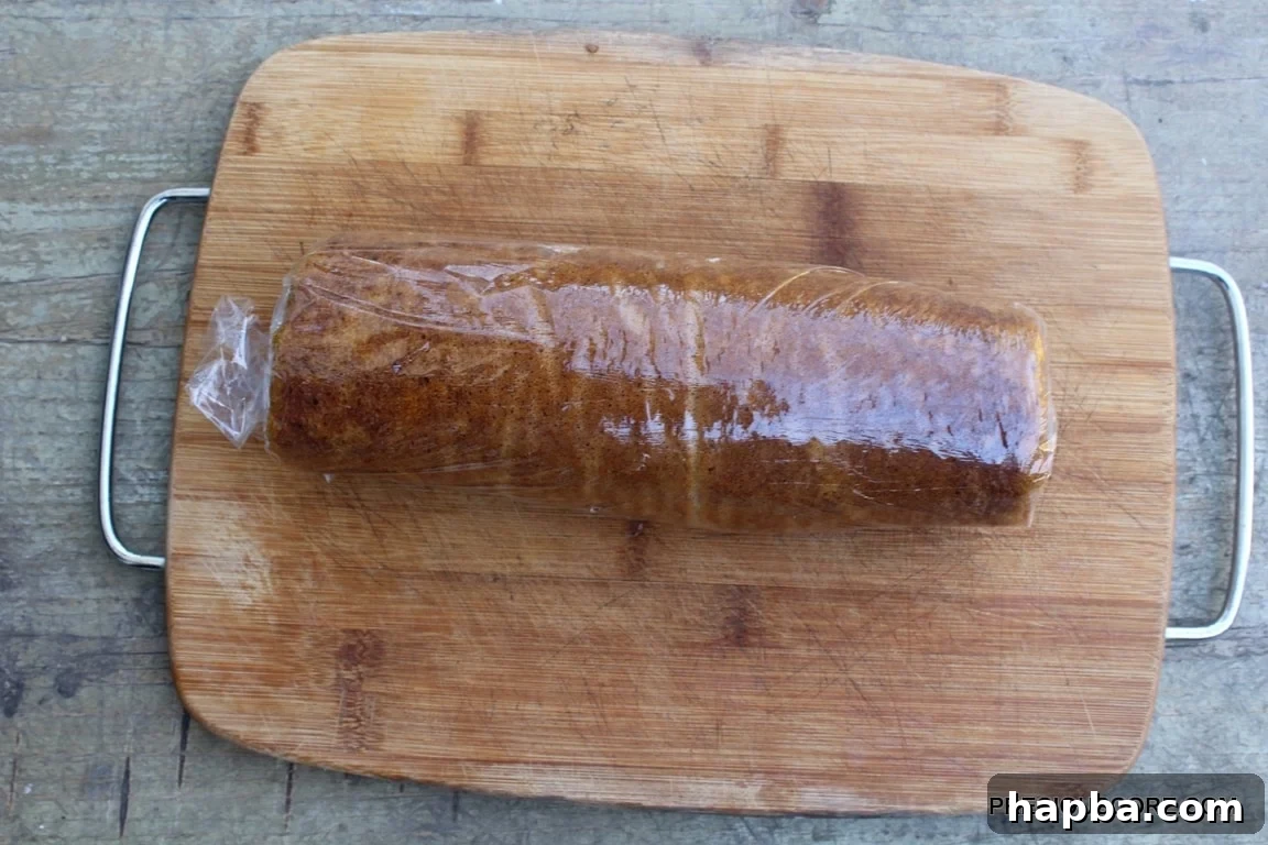 Autumn Spiced Pumpkin Roll 17 Pumpkin cake with cream cheese filling rolled together on a wooden cutting board, ready for chilling.
