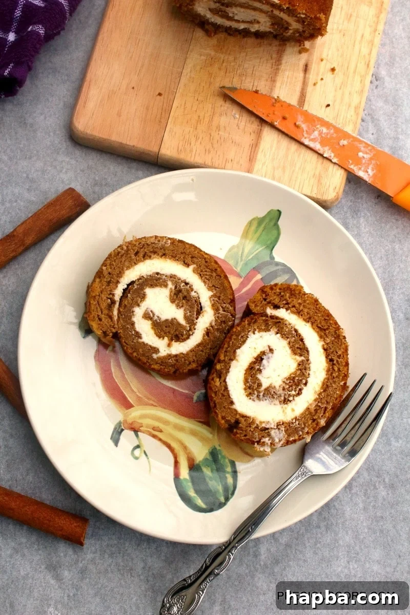 Autumn Spiced Pumpkin Roll 18 Two perfect slices of pumpkin roll cake on a decorated plate with a fork, dusted with powdered sugar.