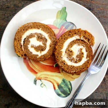 Autumn Spiced Pumpkin Roll 19 Two slices of pumpkin roll cake on a plate with a fork, ready to be enjoyed.