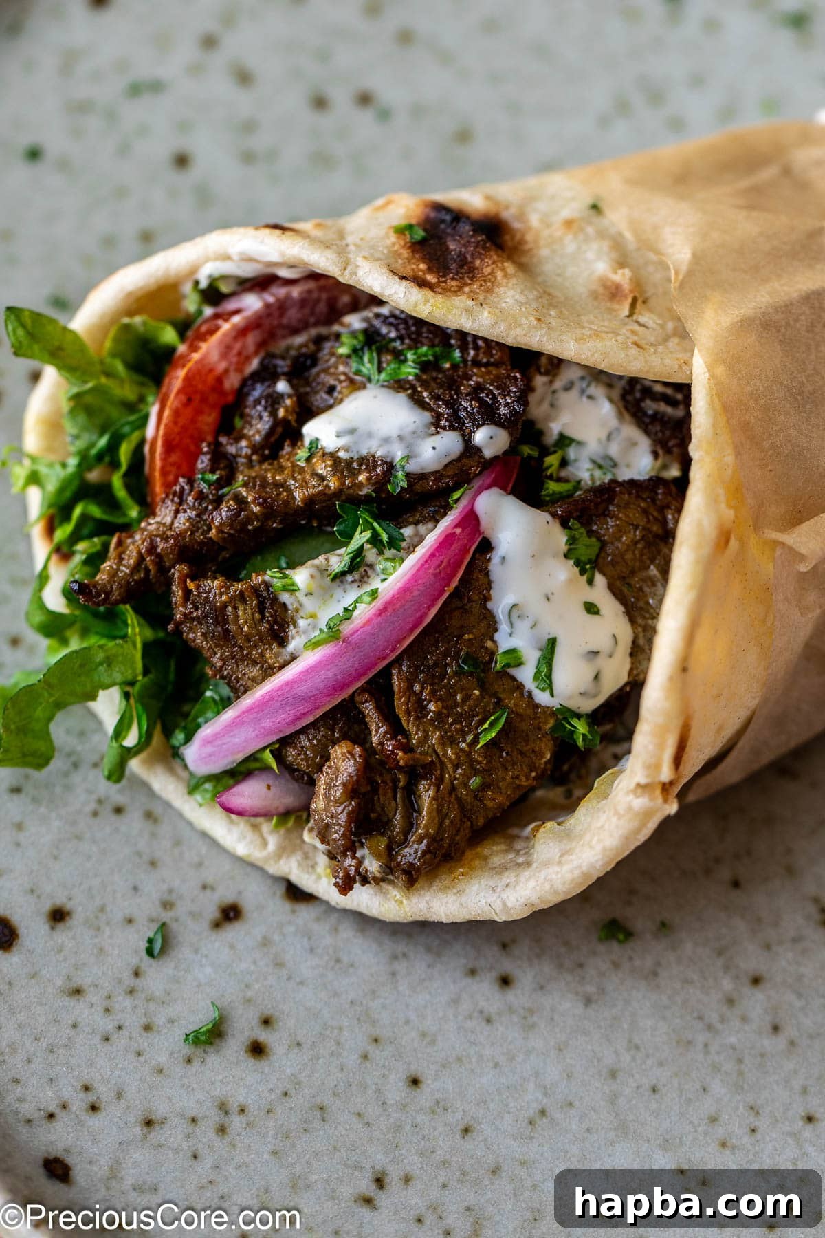 Restaurant-Style Beef Shawarma at Home 10 A beef shawarma wrap filled with vibrant veggies and drizzled with sauce.