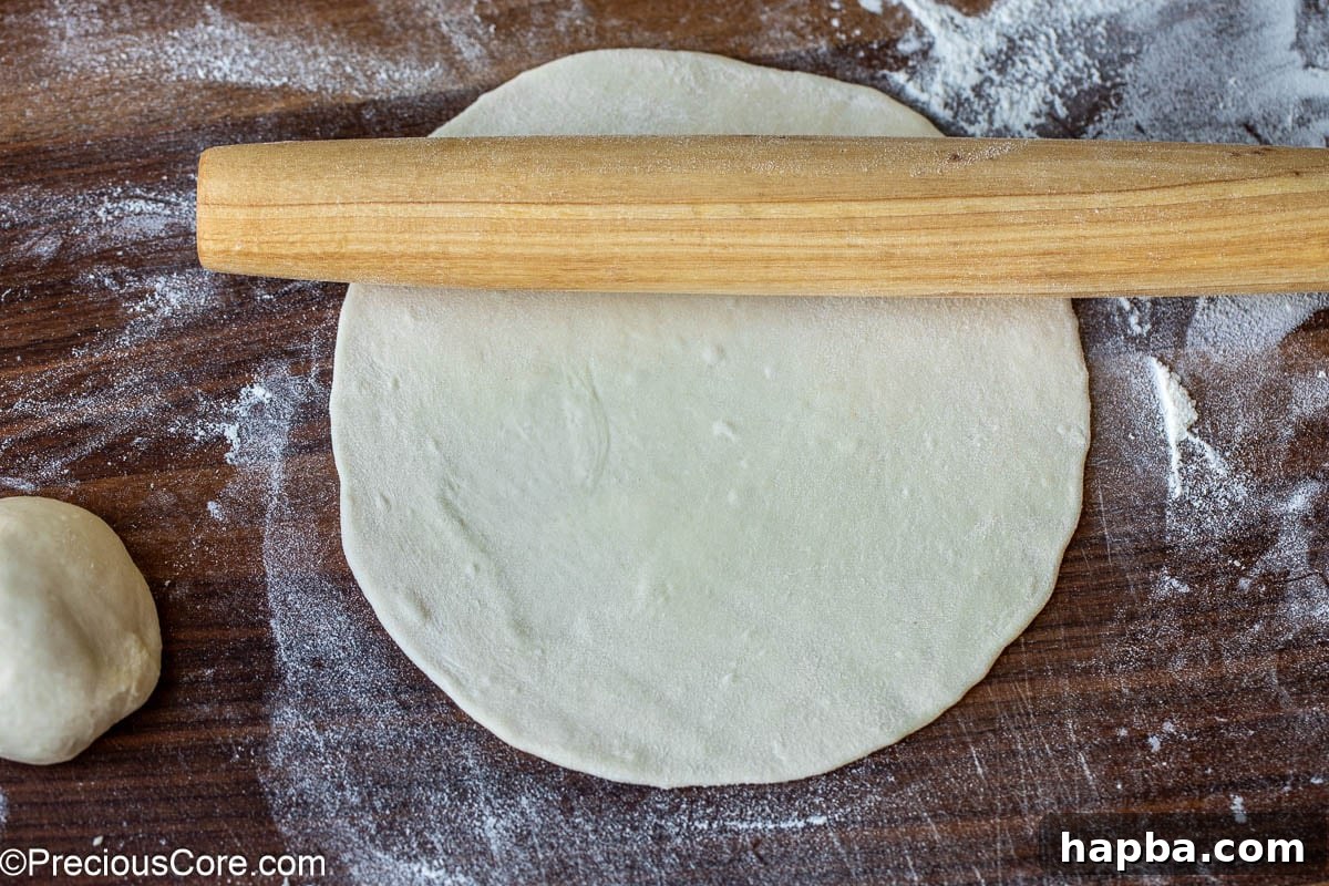 Shawarma Flatbread 9 A rolling pin in action, flattening a piece of dough on a floured surface into a round shape.