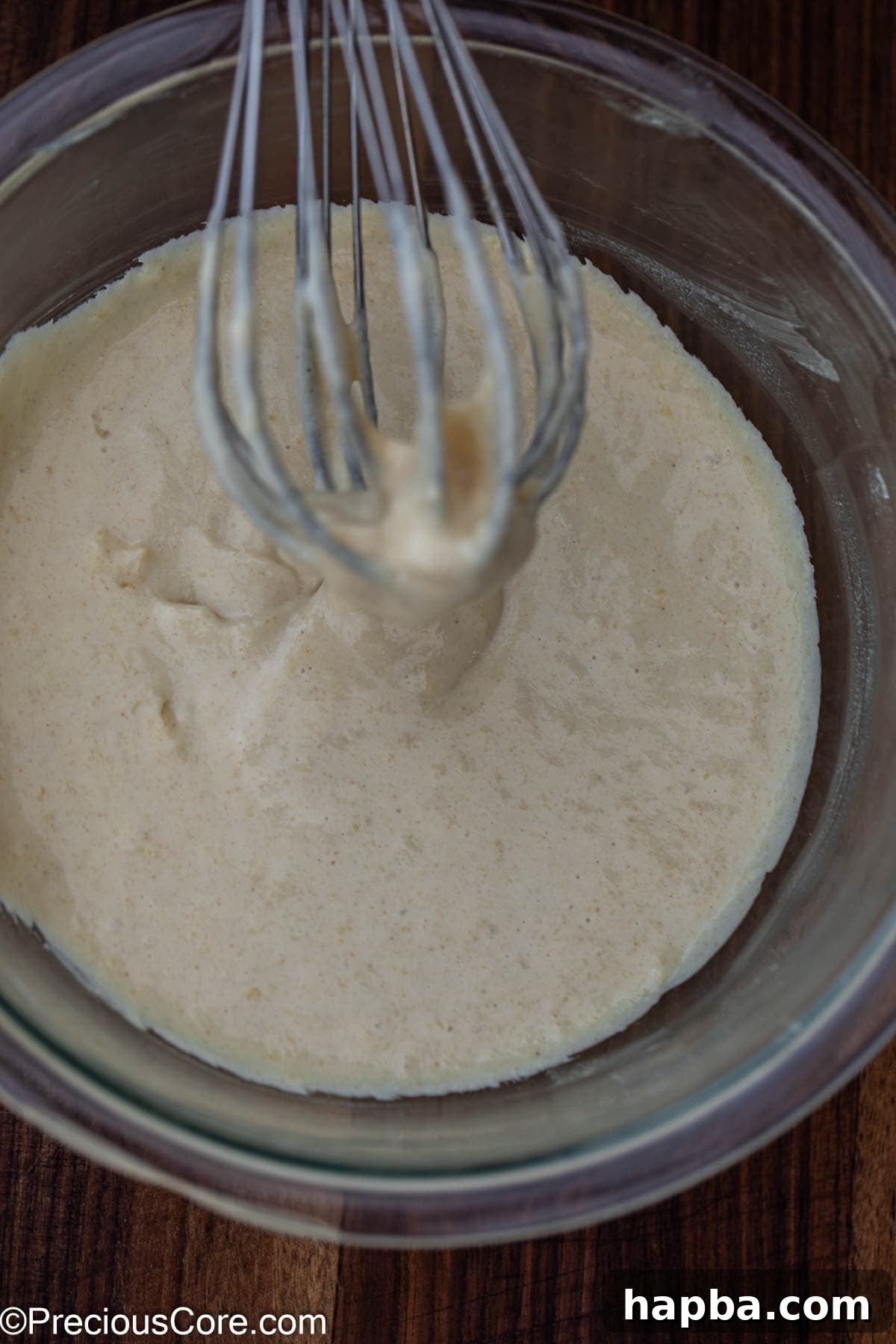 Pancake batter prepared in a white mixing bowl with a whisk, showing a smooth yet slightly lumpy consistency, indicating it's perfectly mixed and ready for making heart shaped pancakes.