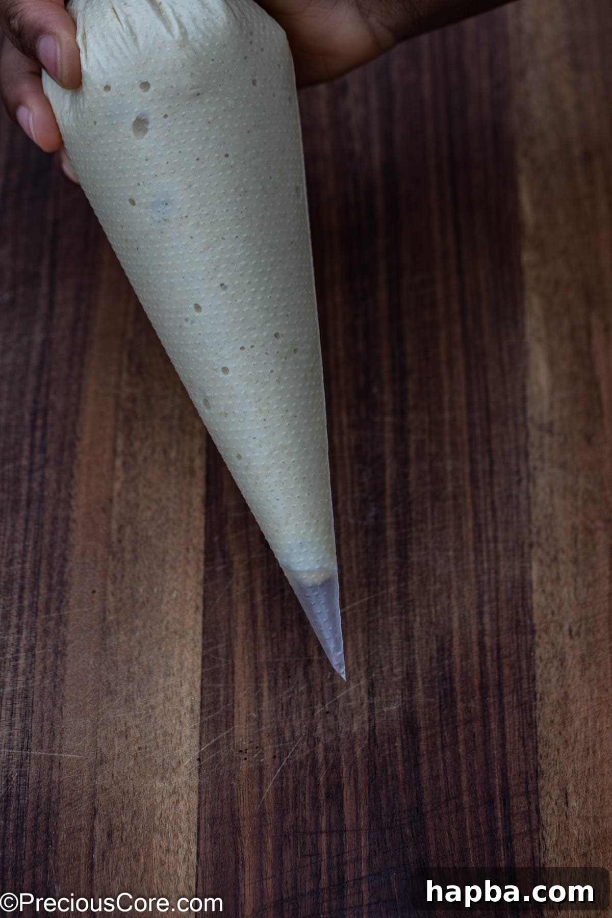 Pancake batter neatly poured into a clear plastic piping bag, with the tip ready to be snipped to the desired size for creating precise heart shapes on the griddle. The bag is held against a blurred kitchen background.