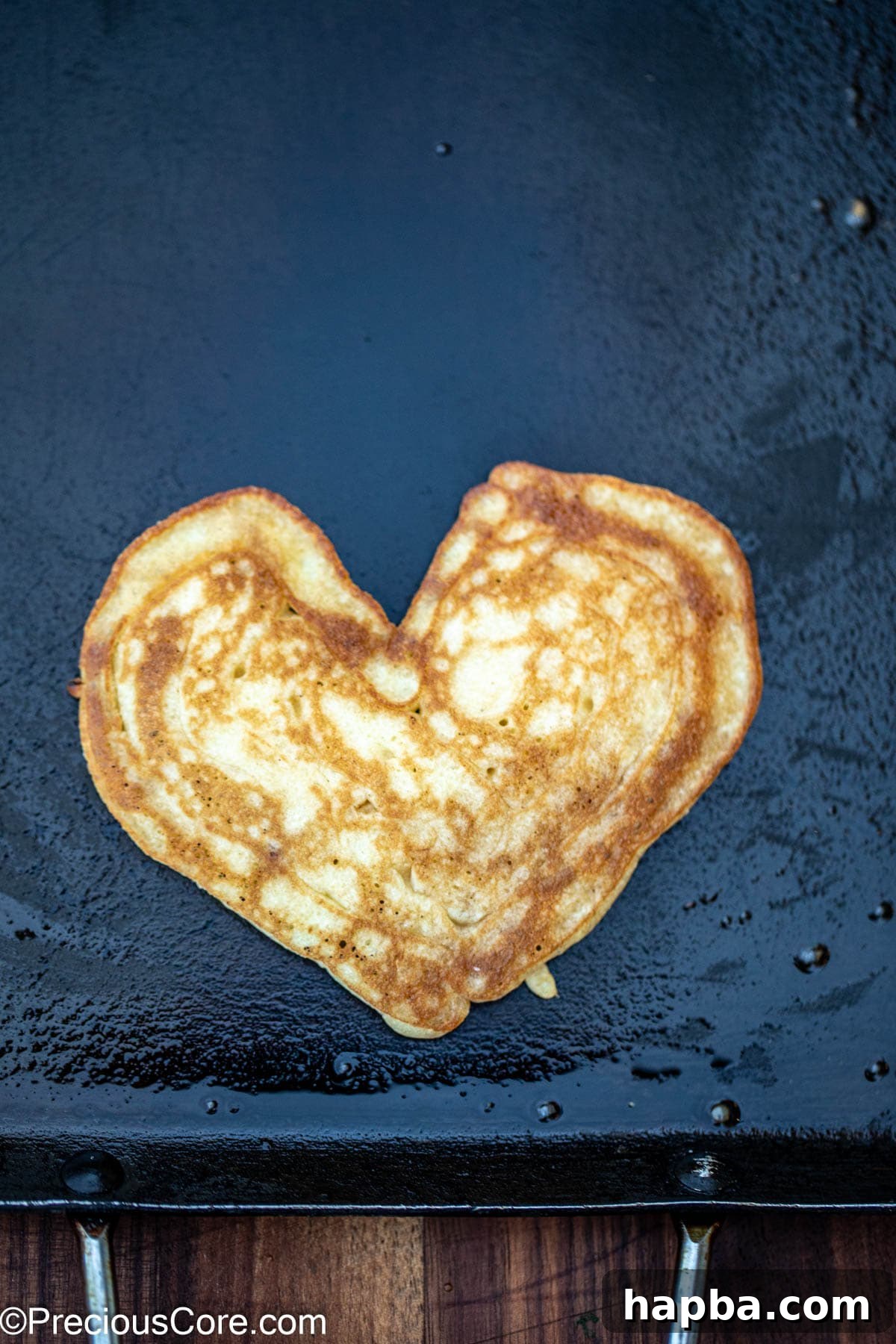 A perfectly cooked, golden brown heart shaped pancake resting on a griddle, showcasing its delightful shape and inviting fluffy texture, ready to be removed and served.
