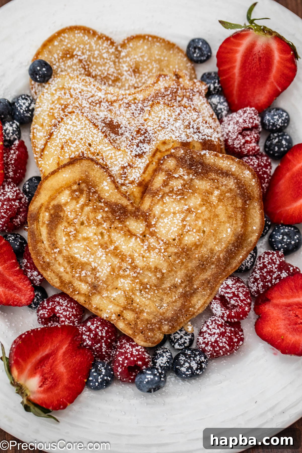 A beautifully arranged plate featuring a stack of three perfectly cooked heart shaped pancakes, adorned with fresh vibrant strawberries and a delicate drizzle of golden syrup, emphasizing their lovely form and inviting appeal.