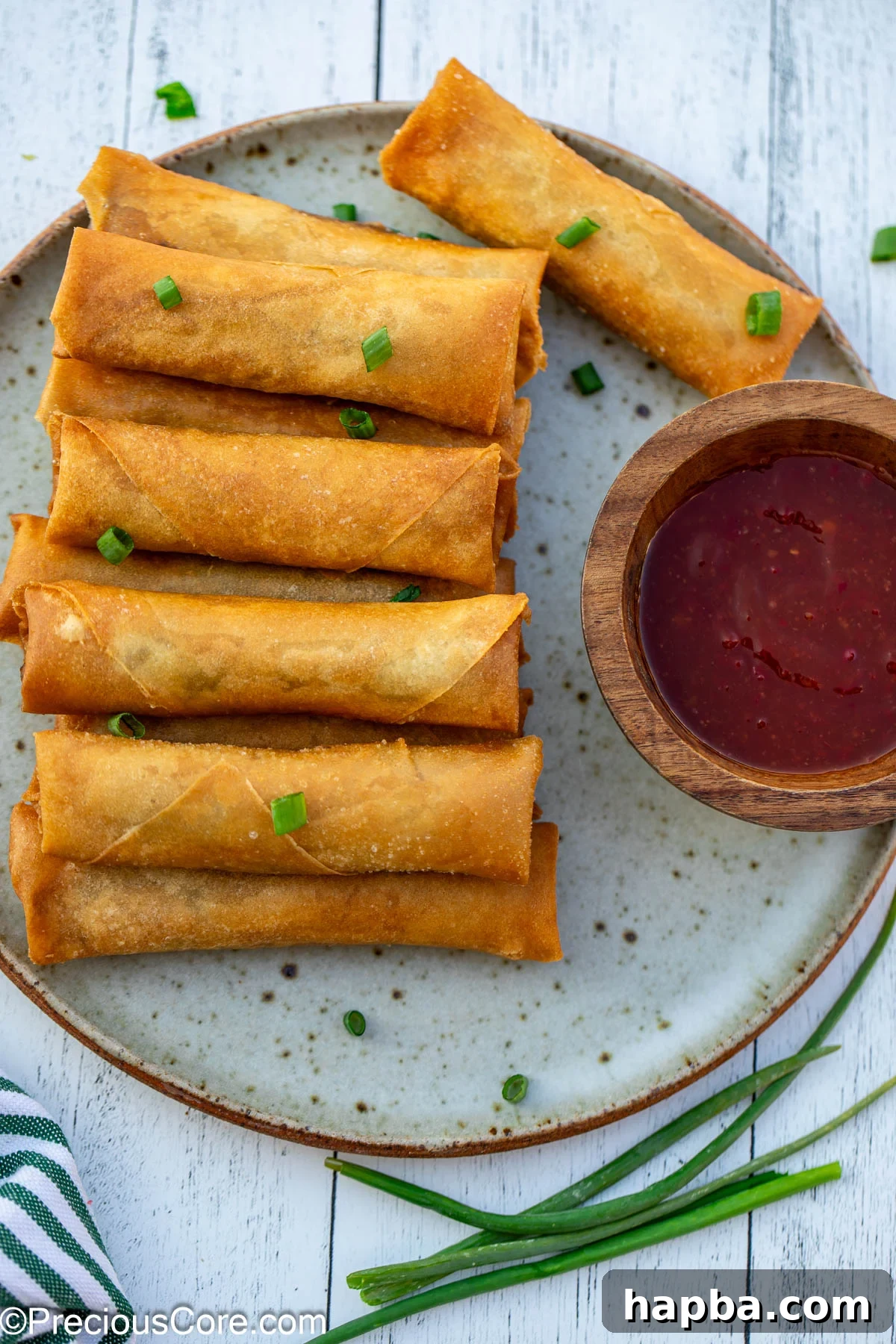 Golden brown spring rolls on a plate, with a bowl of dipping sauce.