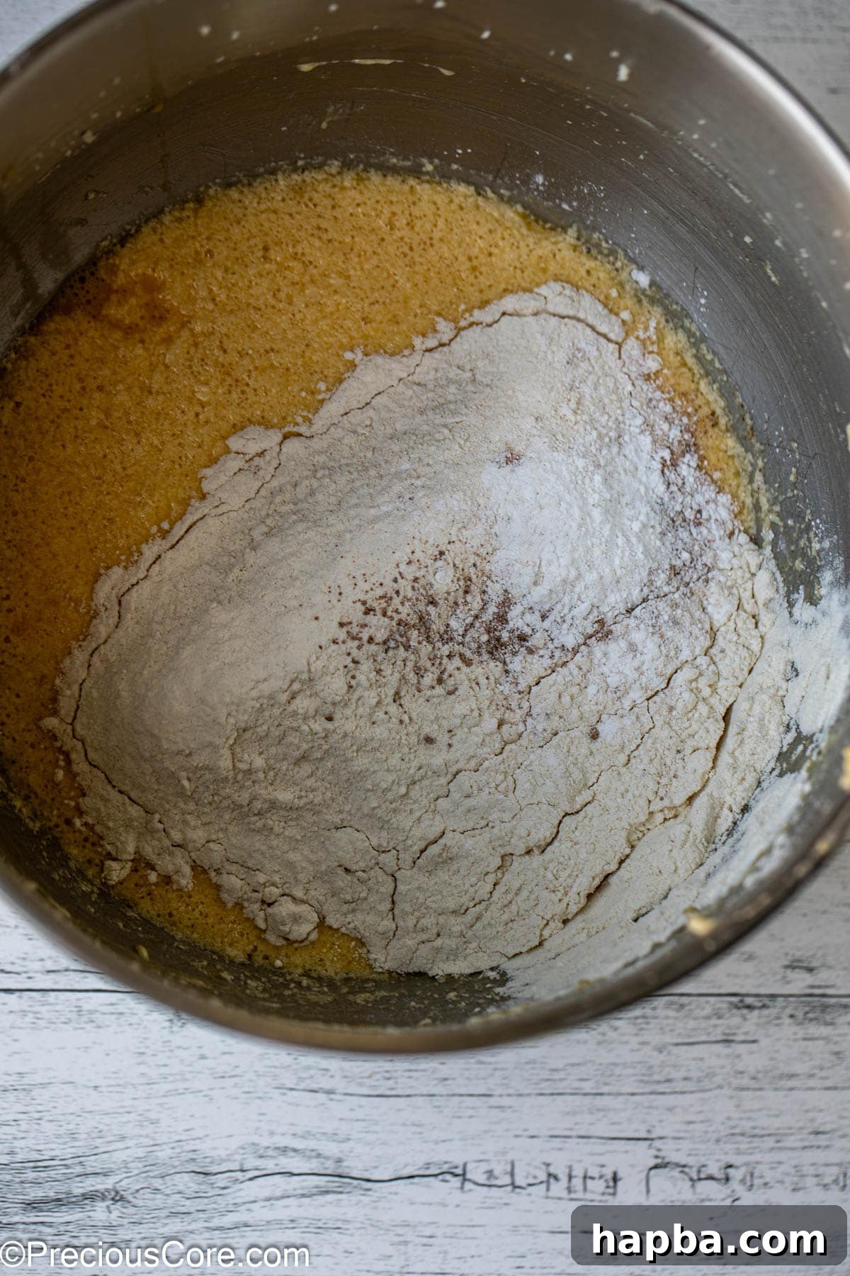 The first portion of dry ingredients, including flour, baking powder, and nutmeg, being gently folded into the smooth cake batter.