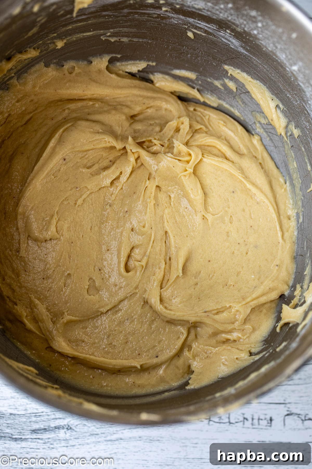 A perfectly smooth and consistent cake batter swirling within a gleaming metal mixing bowl, ready for baking.