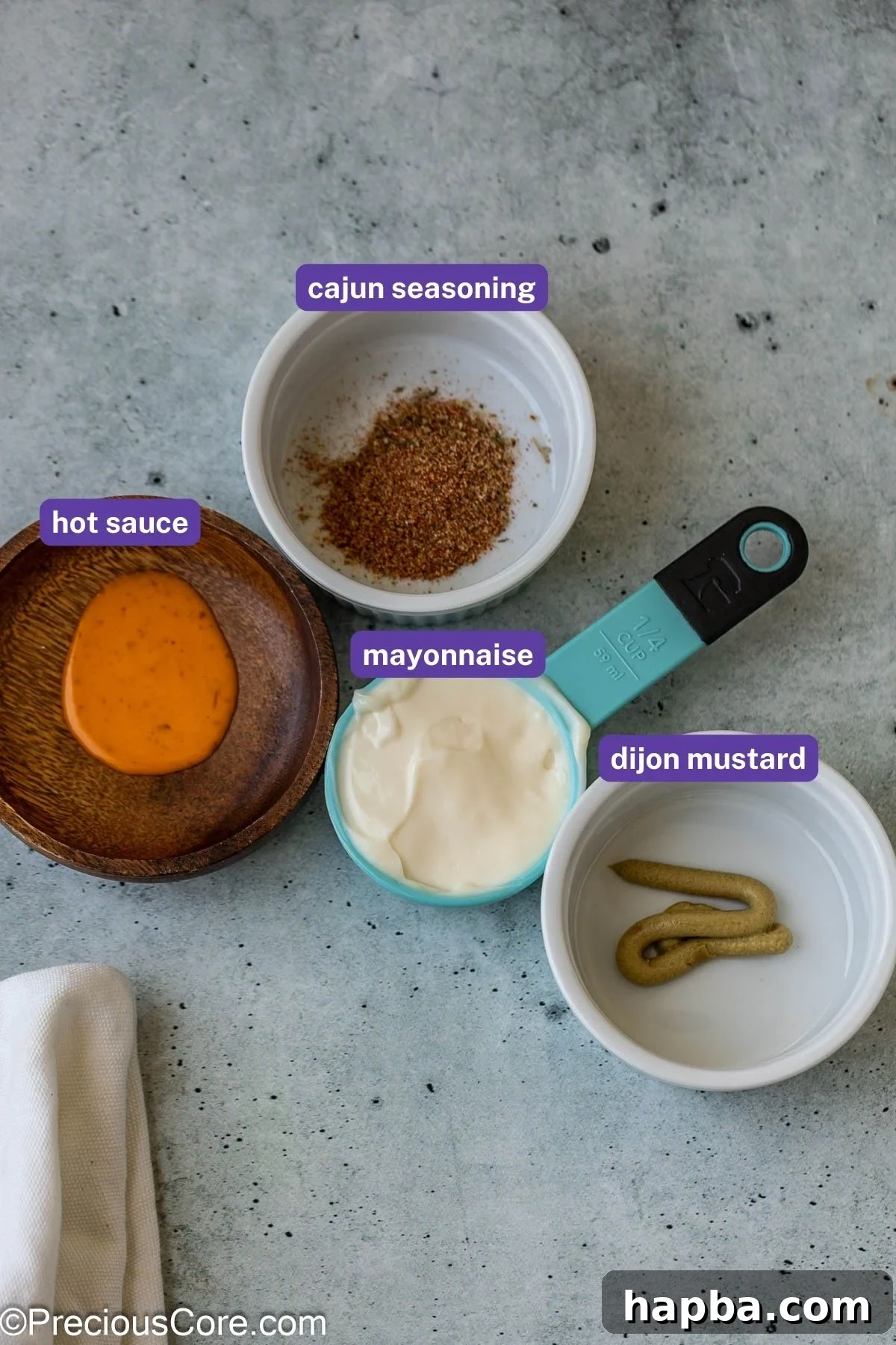 Measured ingredients for the homemade mayonnaise sauce, including mayonnaise, hot sauce, Dijon mustard, and Cajun seasoning.
