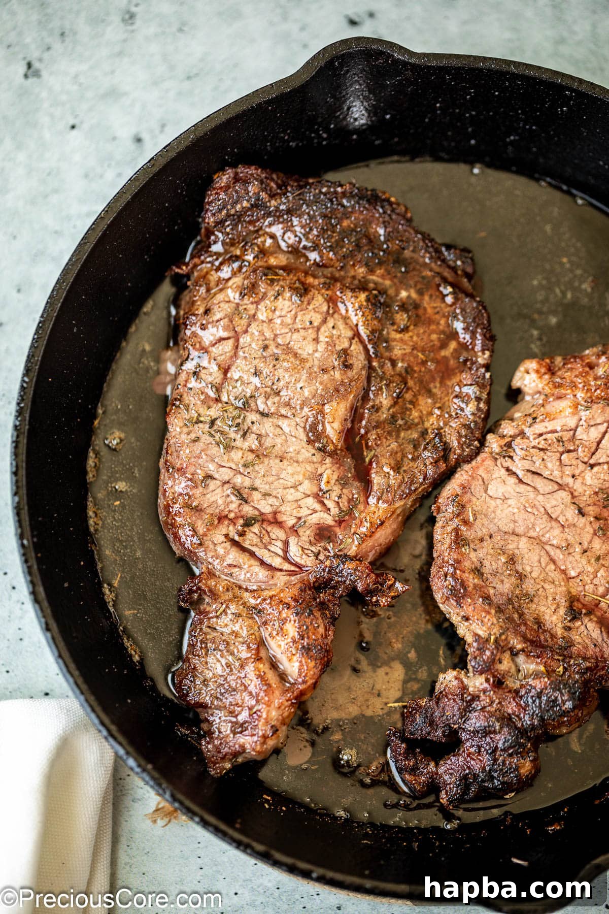 Two ribeye steaks sizzling in a hot cast iron skillet, developing a perfect crust.