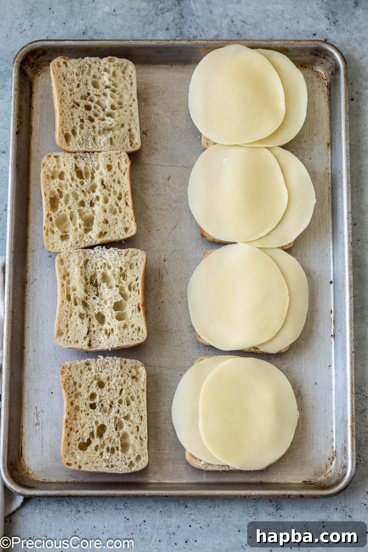 Ciabatta rolls sliced in half with provolone cheese slices arranged on the bottom halves, ready for the oven.